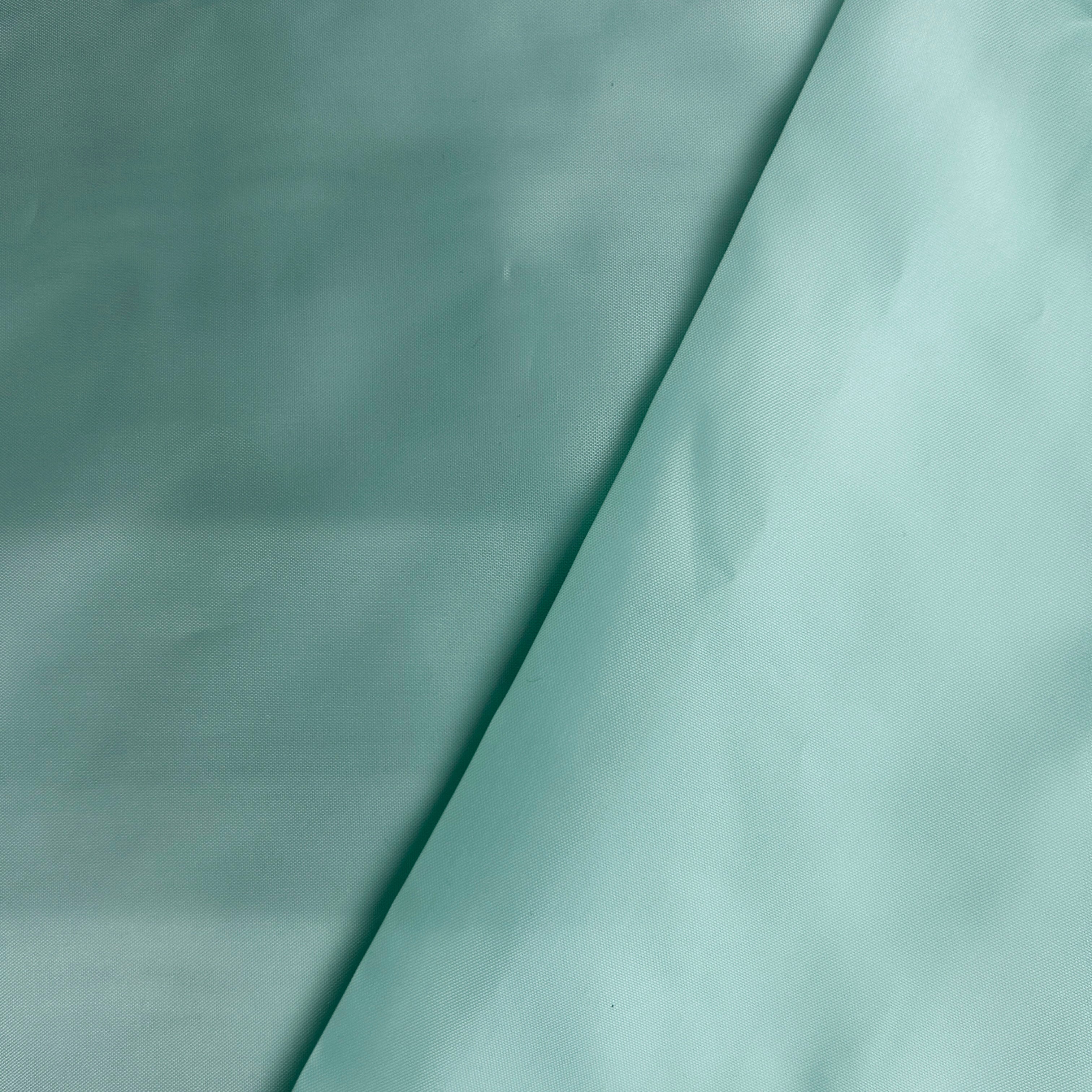 A close-up of a light mint green or pale aqua fabric surface with soft folds and shadows, filling the frame.
