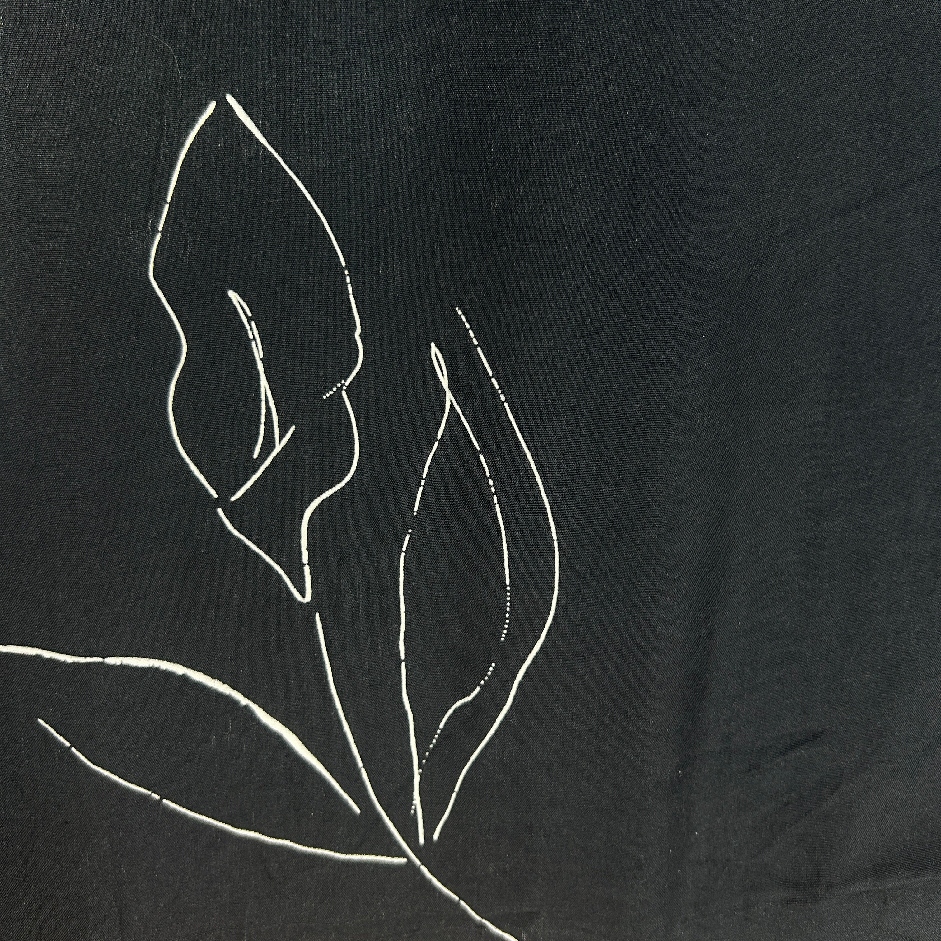 A close-up of a black fabric surface with a simple white line drawing of a flower bud and leaf.