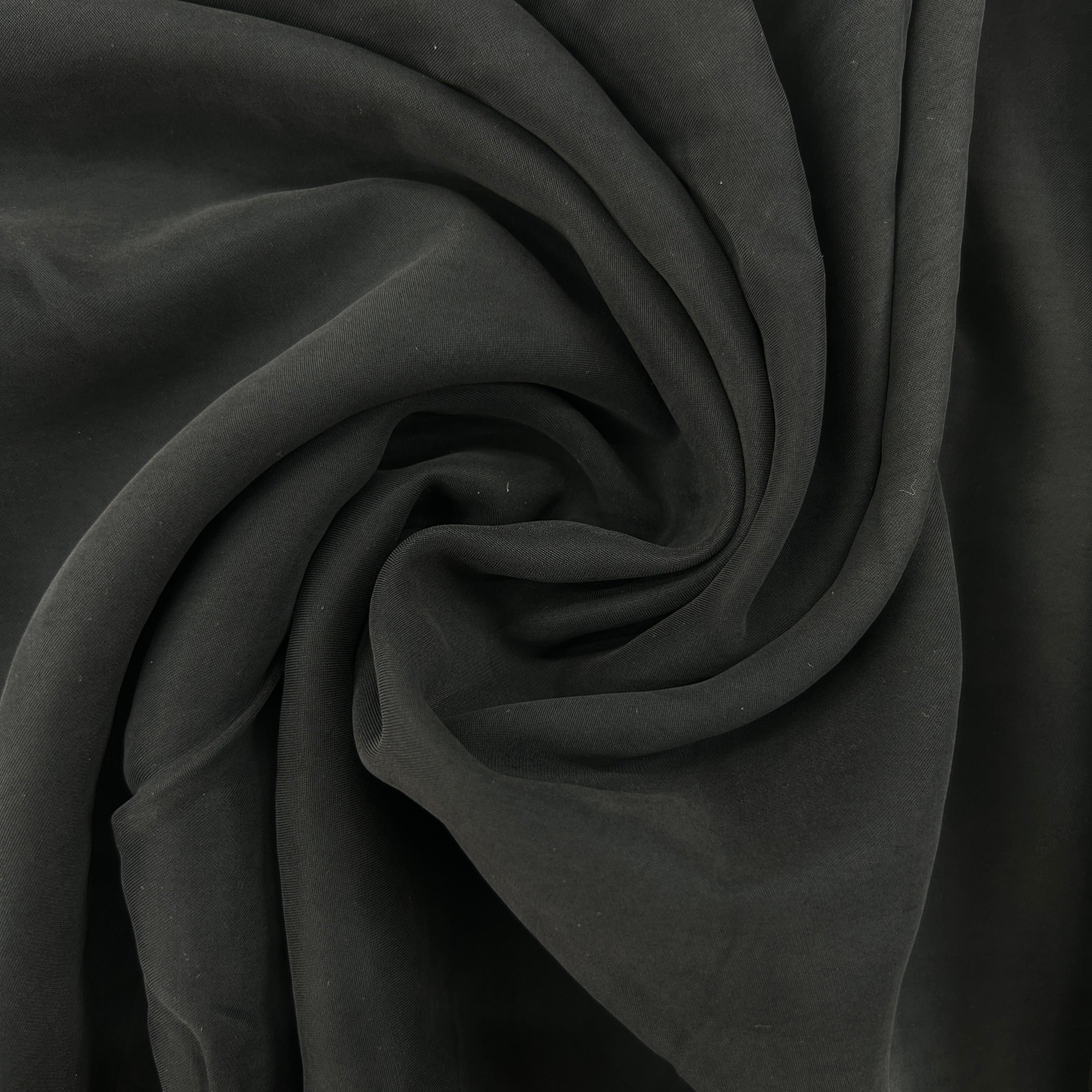 A close-up of draped dark charcoal gray fabric arranged in a spiral swirl, showing its soft texture and matte finish.