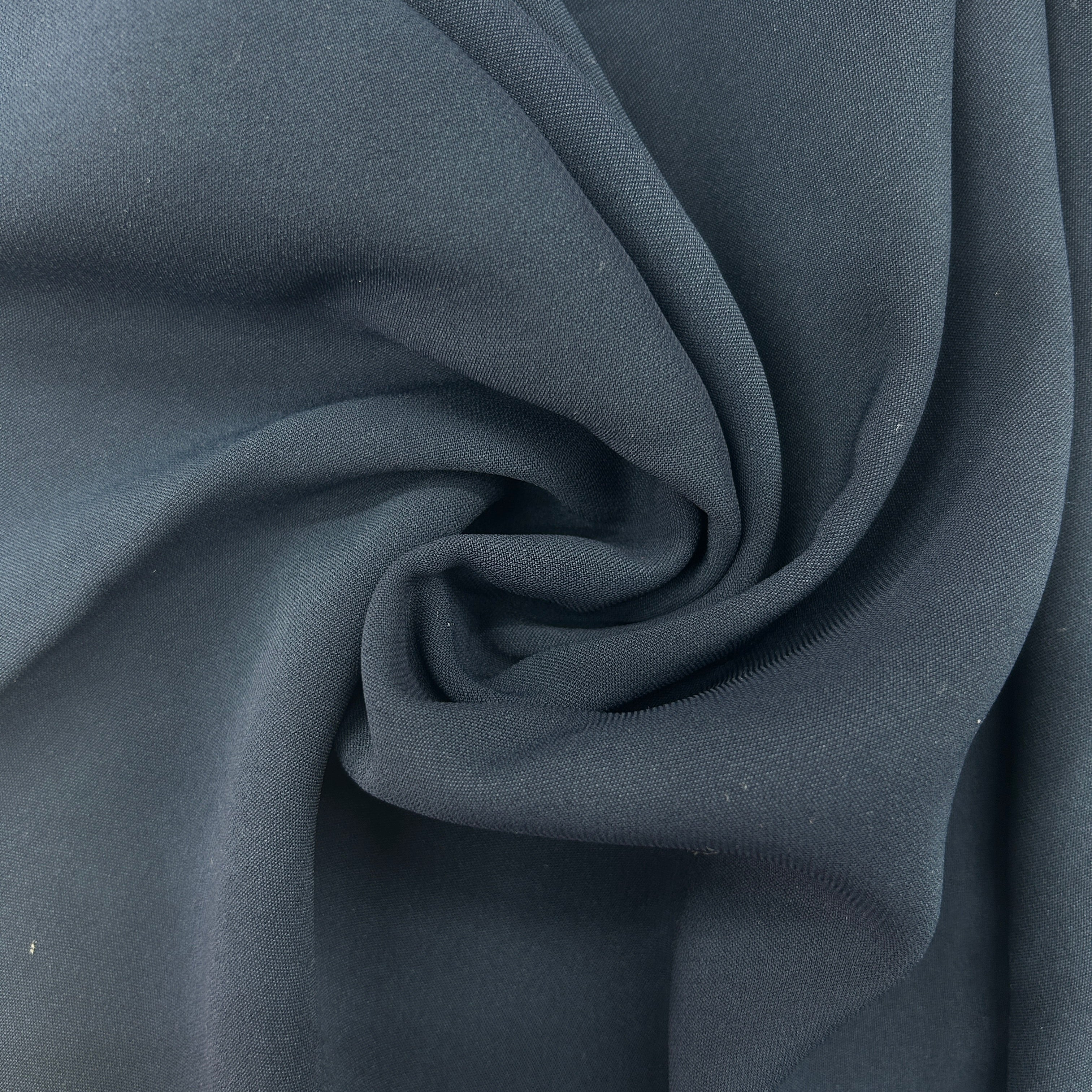 A close-up of draped dark slate gray fabric with a soft, matte texture, arranged in a central swirl.