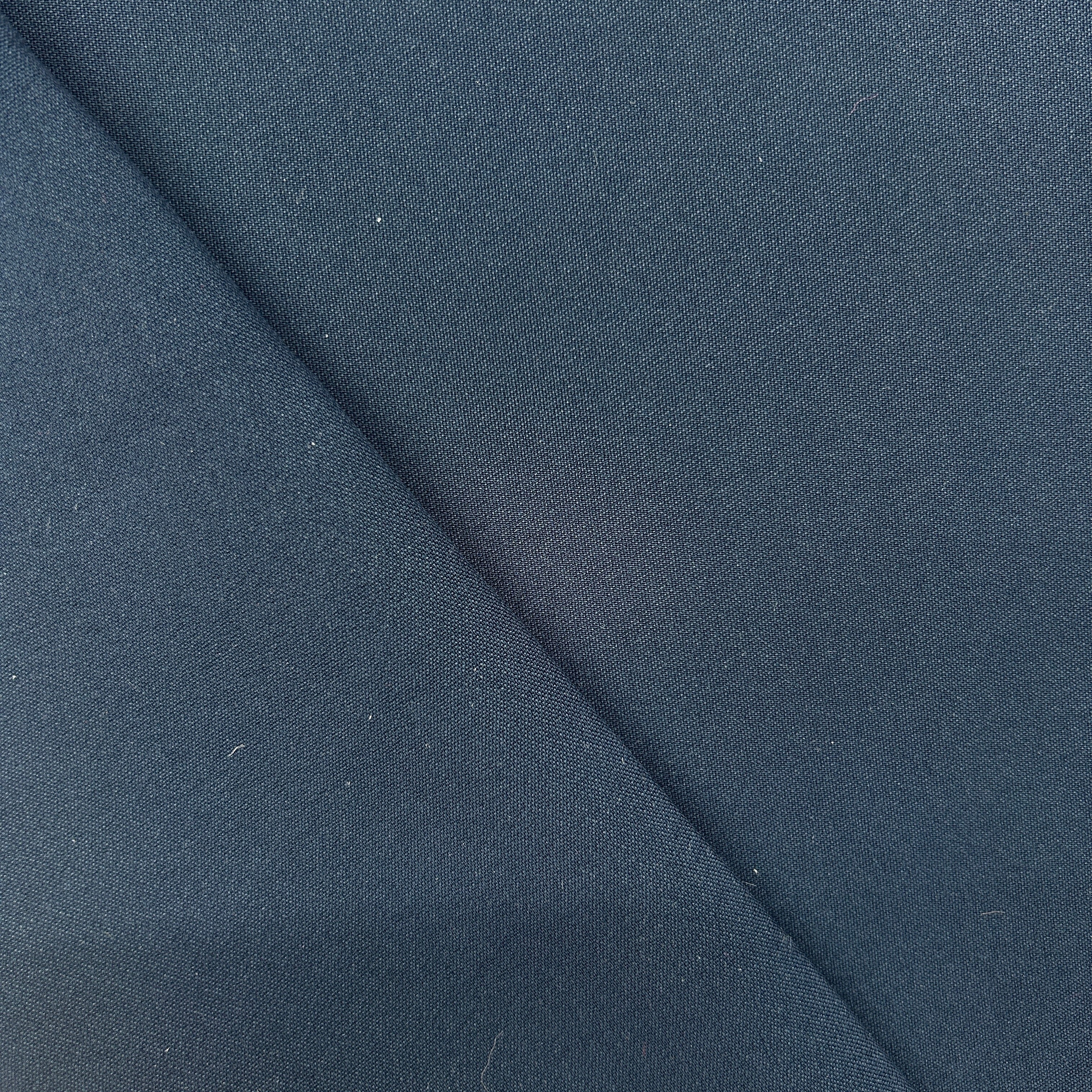 A close-up of dark navy blue fabric with a diagonal fold creating a soft shadow.