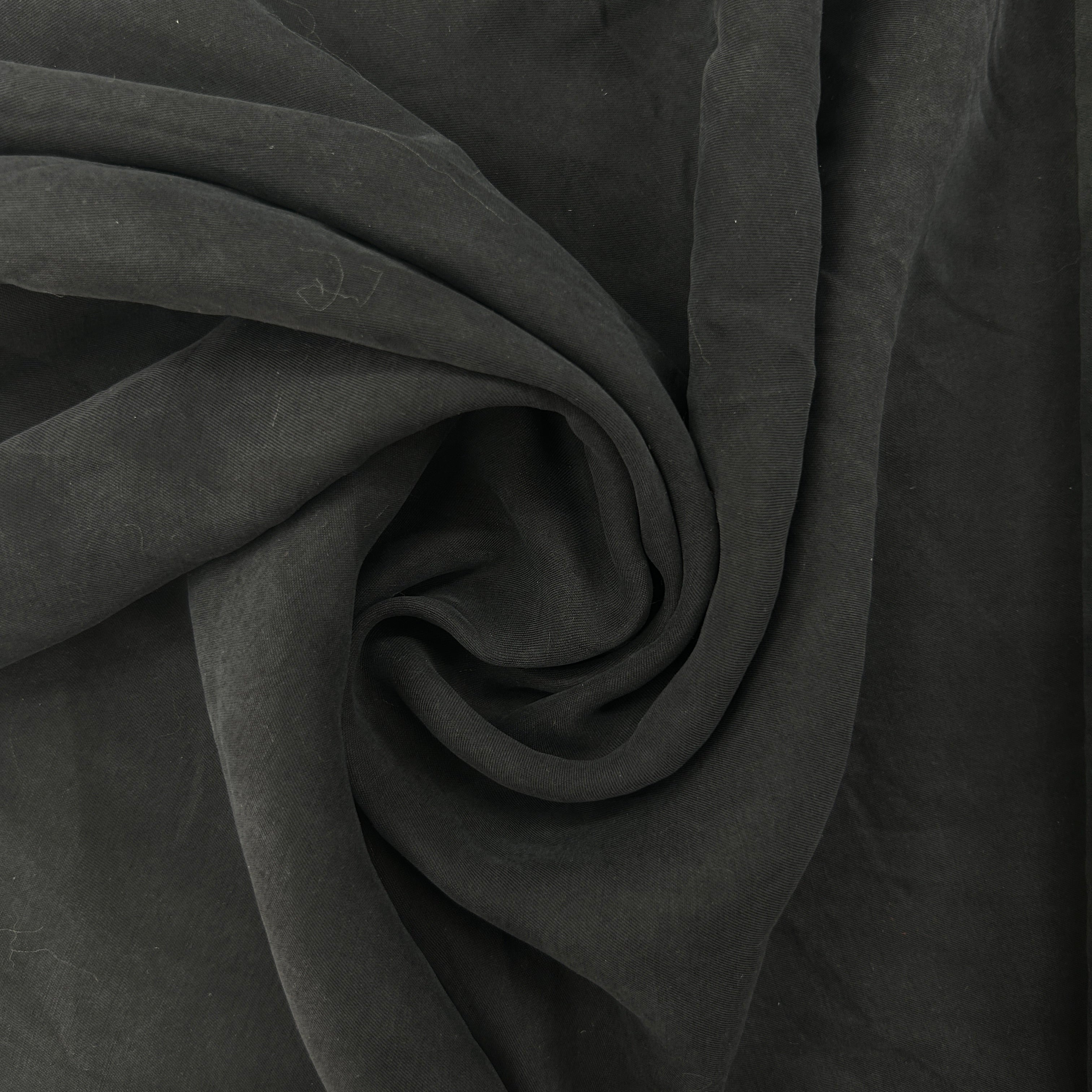 A close-up of dark charcoal gray fabric draped in a spiral pattern, showing its soft texture and folds.