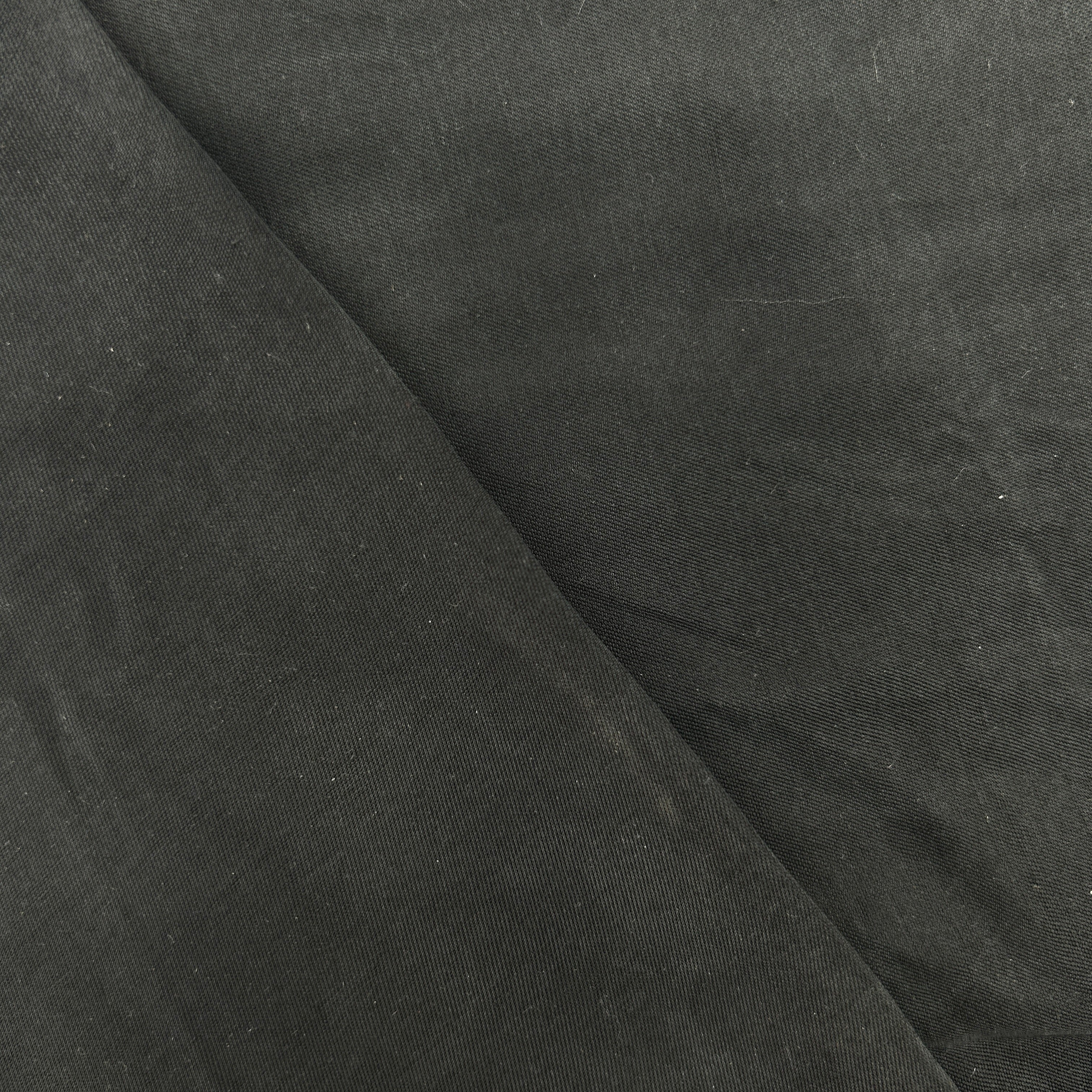 A close-up of dark charcoal gray fabric with a diagonal fold creating a textured pattern.