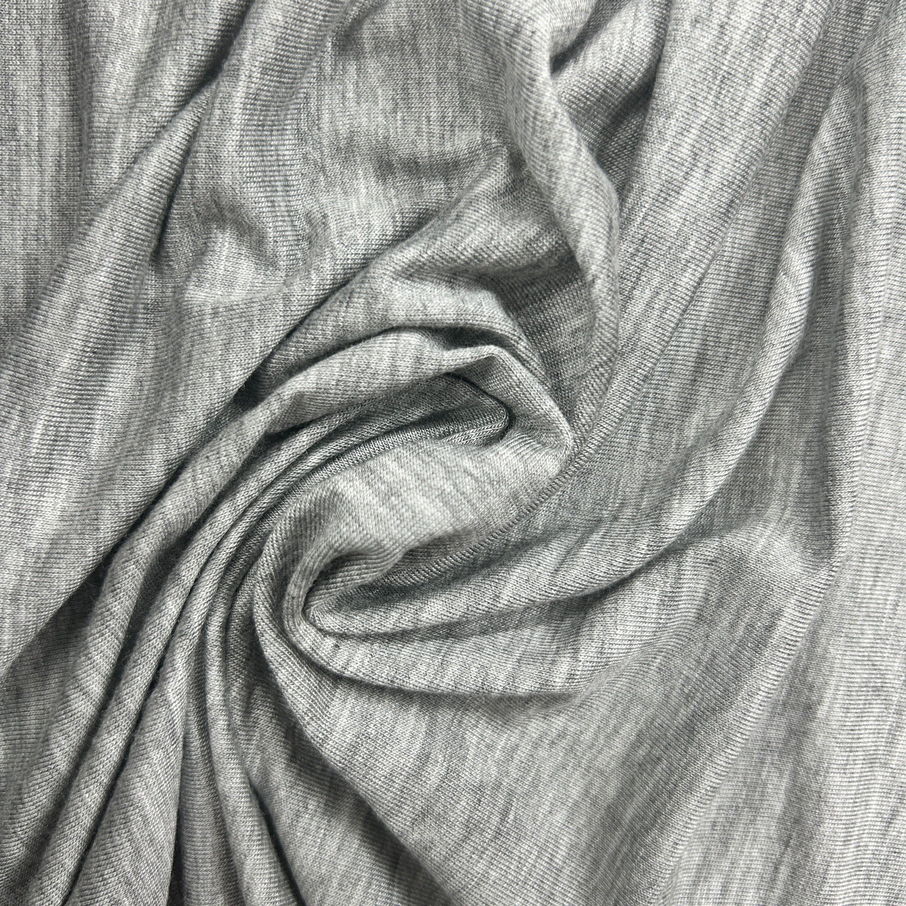 A close-up of draped gray fabric with a fine textured weave, arranged in soft folds that show the material's drape and color.