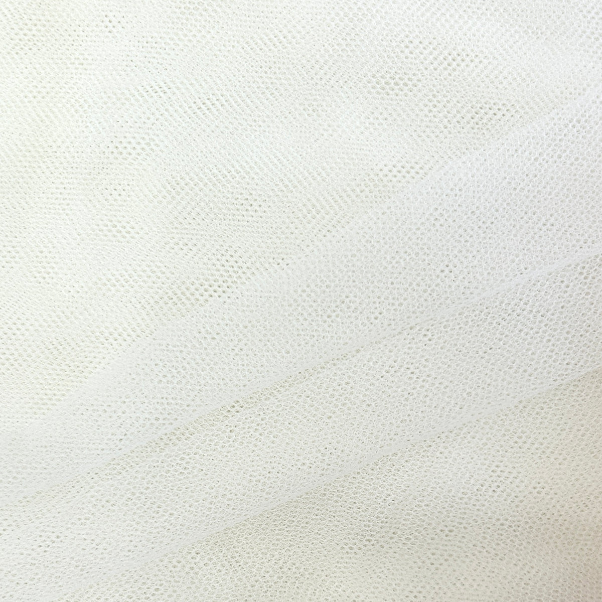 A close-up of white mesh fabric with a fine dotted texture and soft diagonal folds.