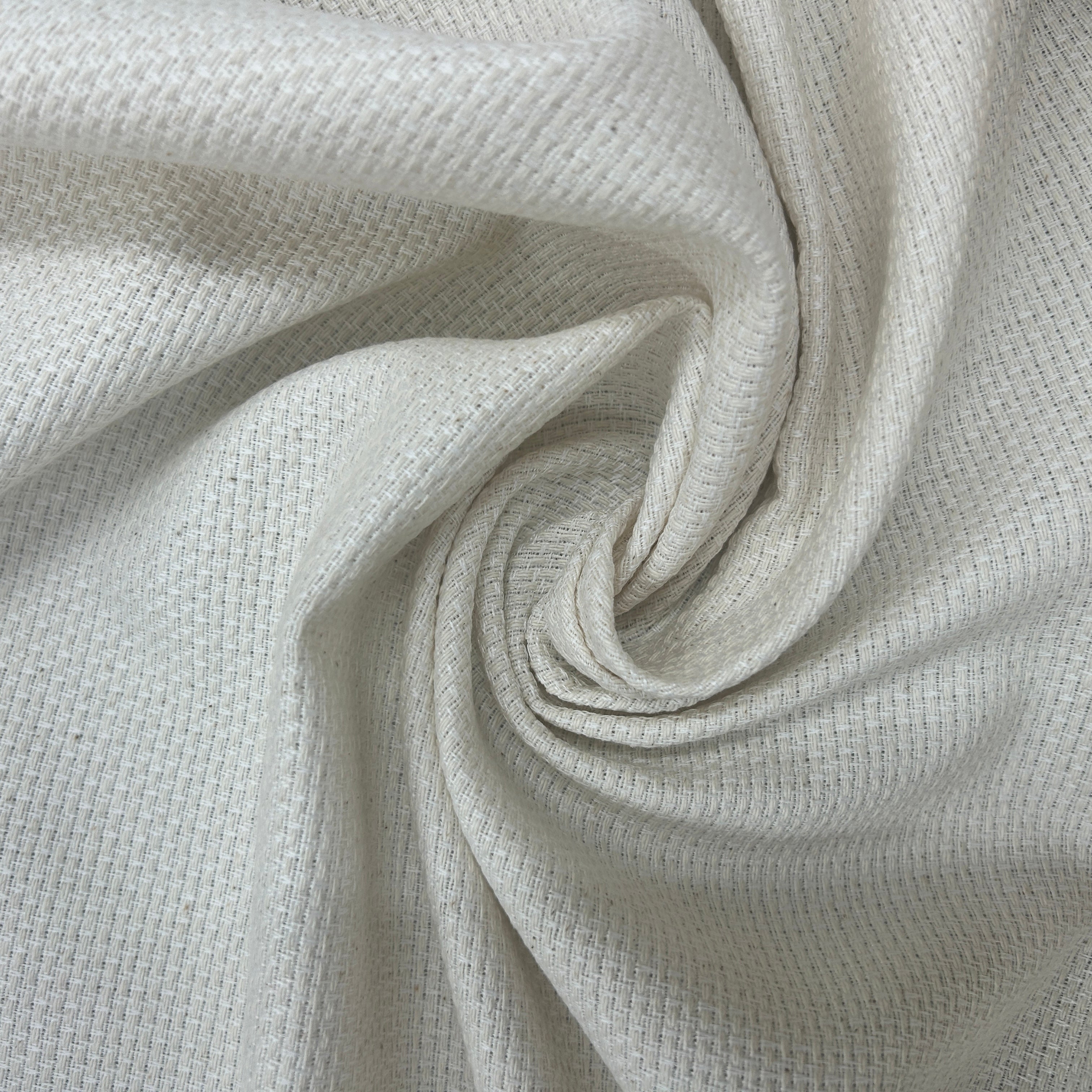 A close-up of a textured cream-colored fabric swirled in a spiral pattern, showing its fine woven details.