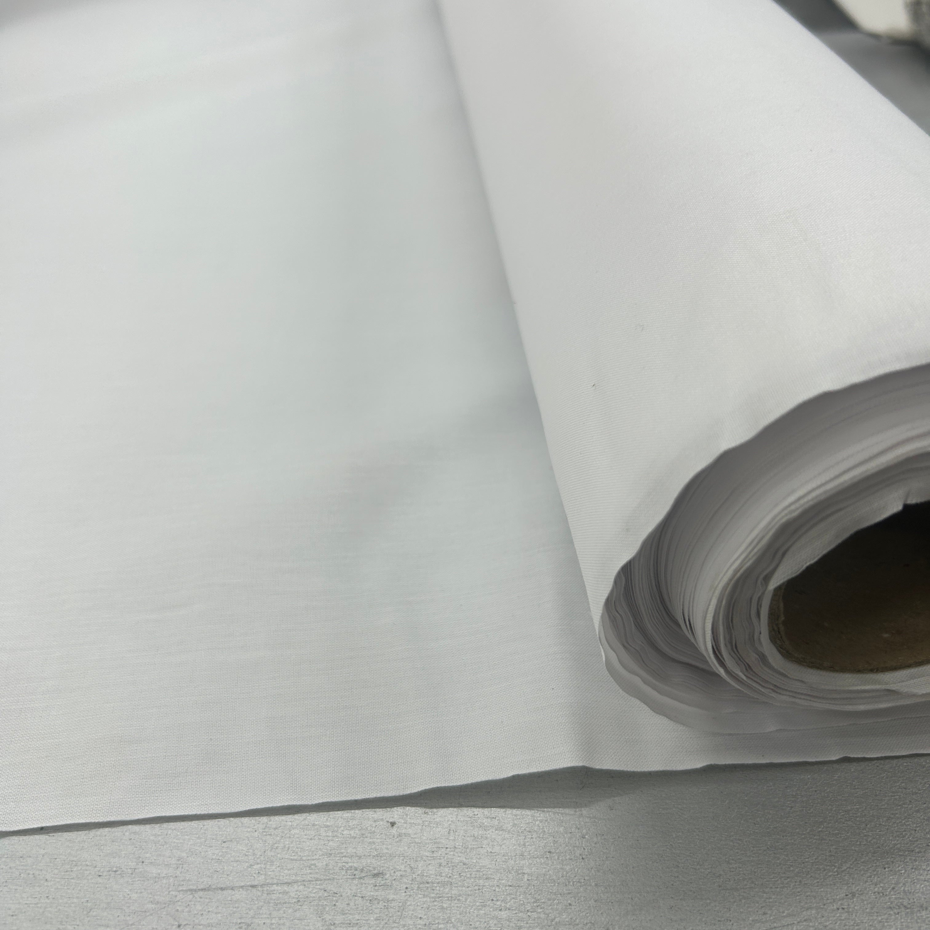A close-up of a white roll of fabric or paper, partially unrolled, showing its texture and layered edges on a gray surface.