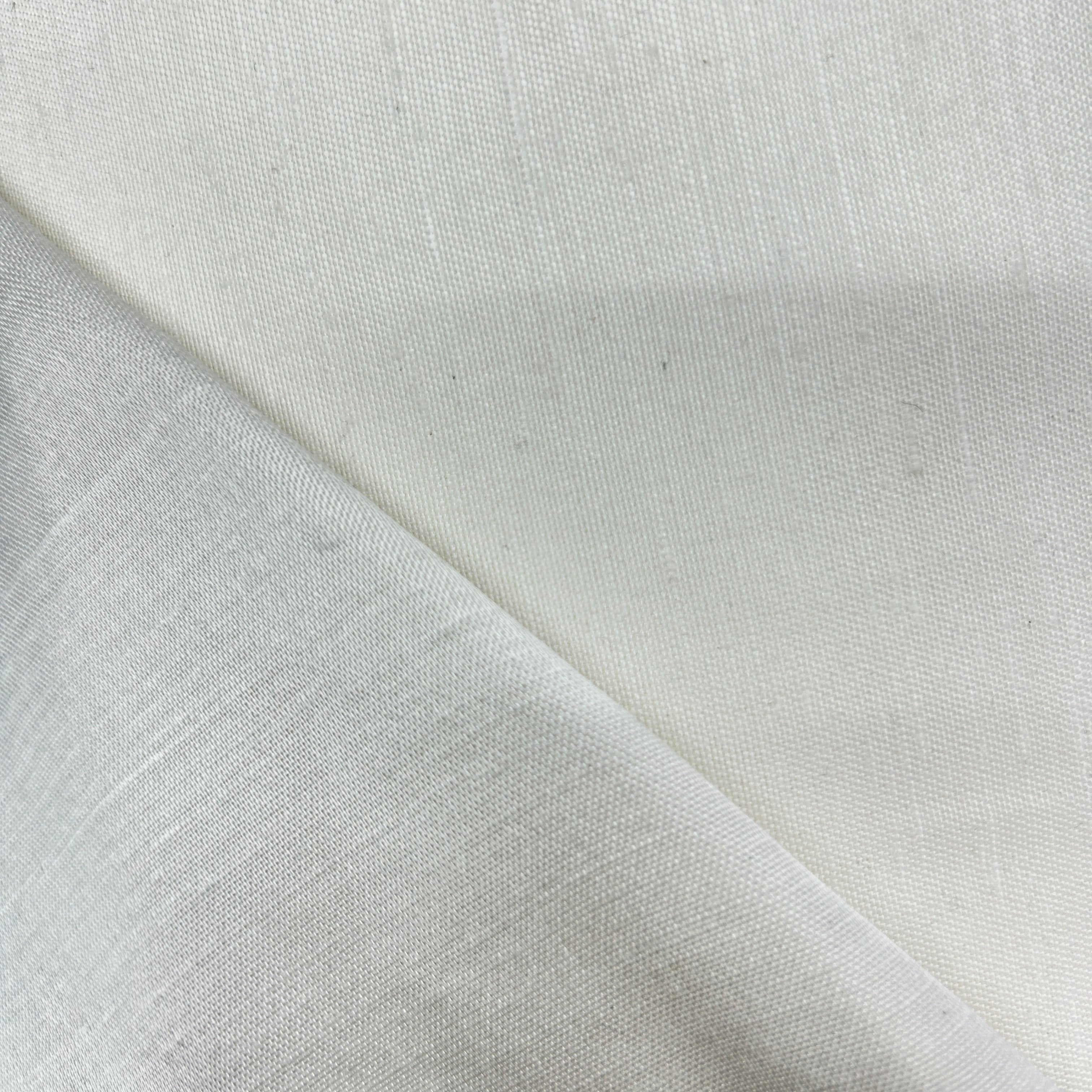 A close-up of off-white woven fabric with a visible diagonal fold showing the texture and weave.