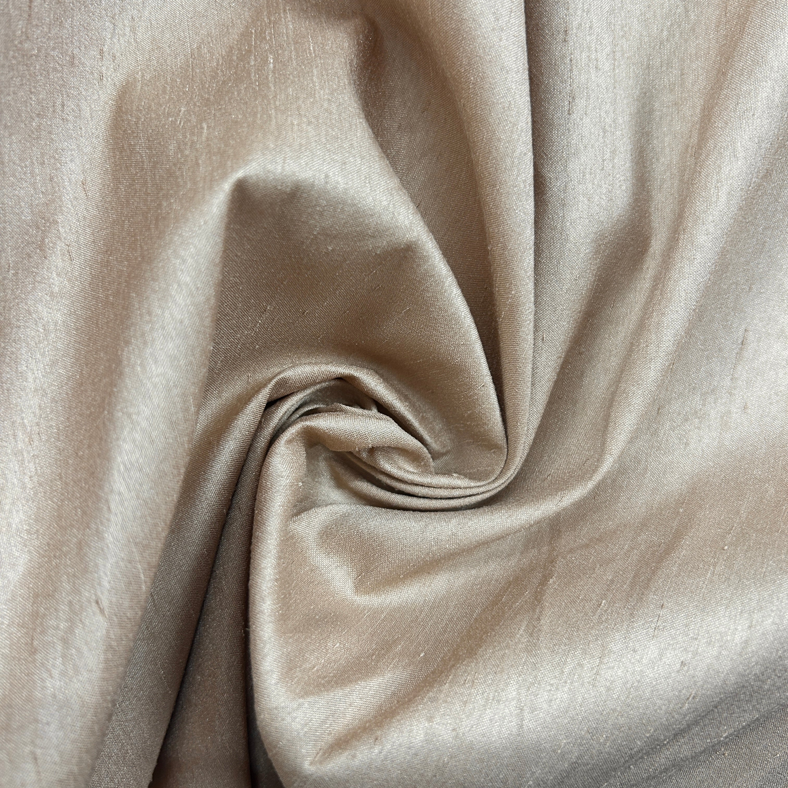 A close-up of draped satin fabric in a warm champagne beige color, showing its soft sheen and texture.