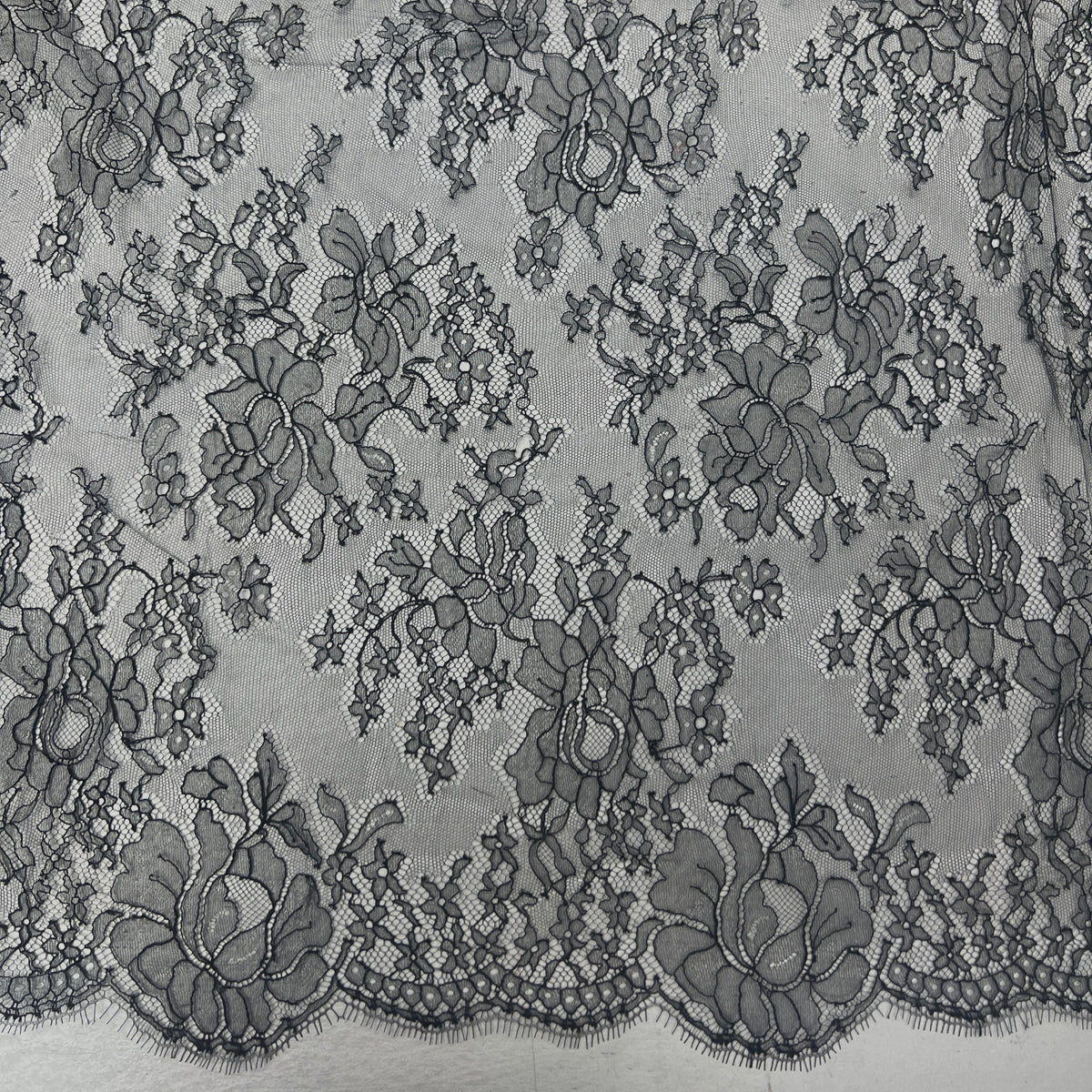Black floral lace fabric with a scalloped edge, shown in a close-up texture view.