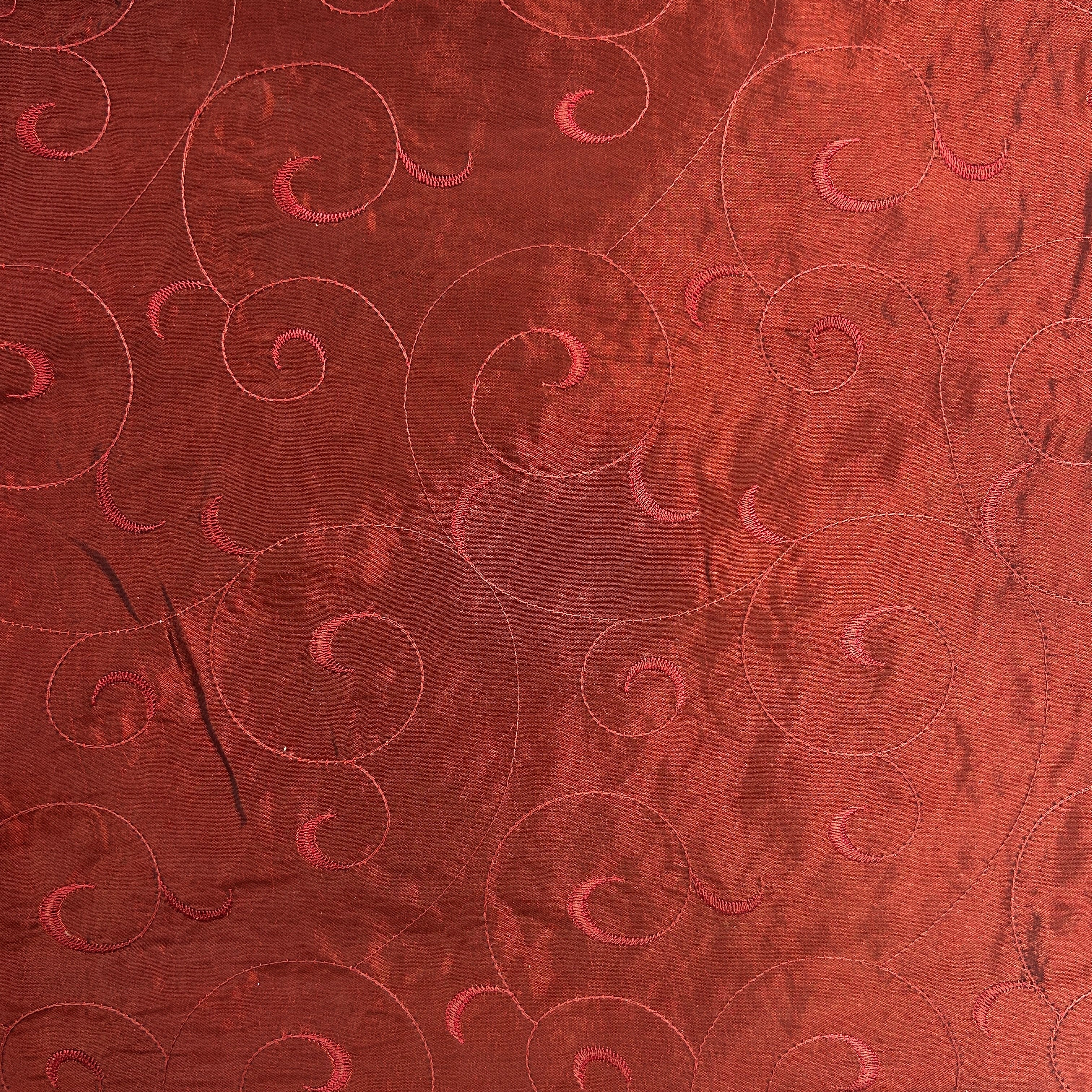 A close-up of a red fabric surface with swirling stitched quilting patterns.