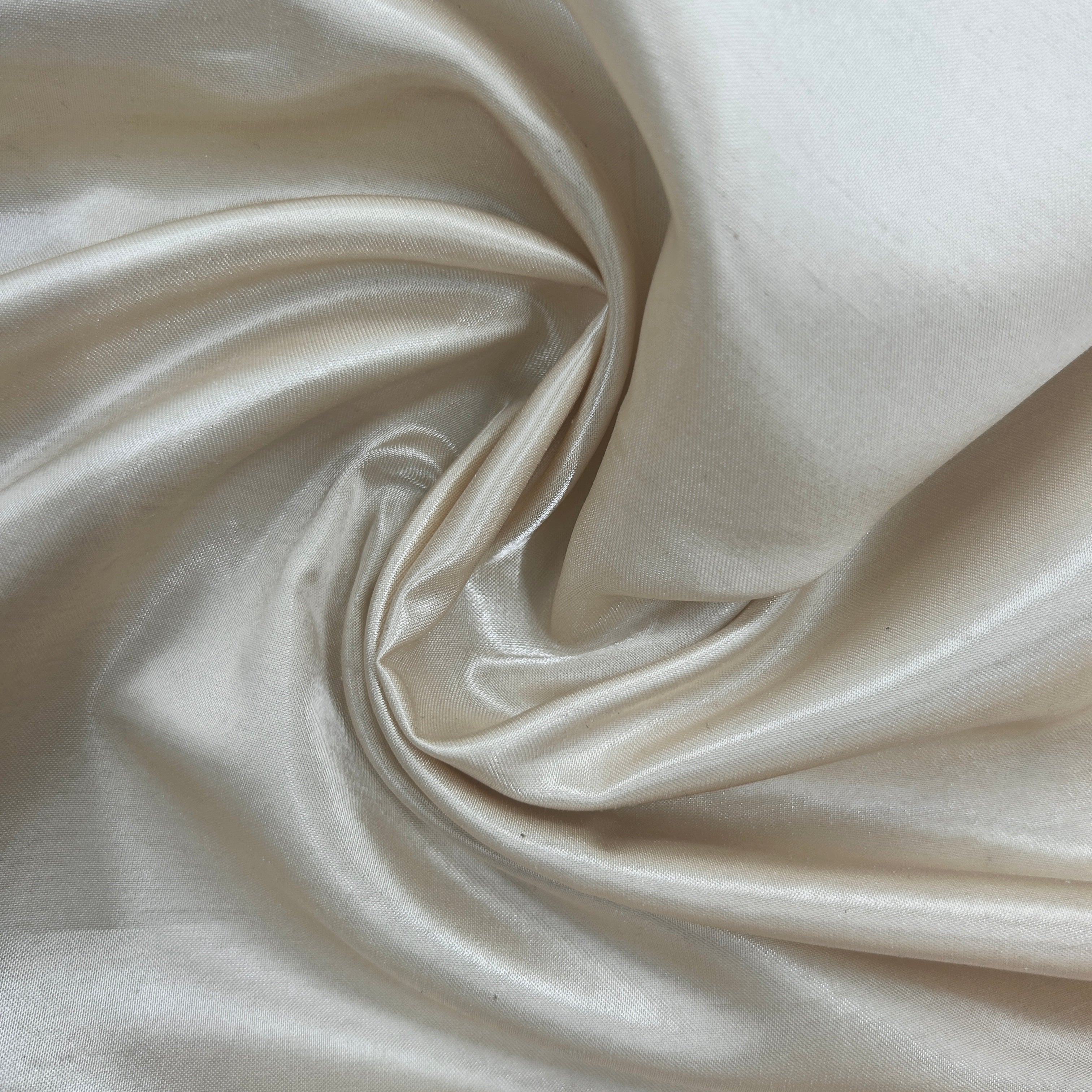 A close-up of draped satin fabric in a warm ivory or cream color, showing its smooth texture and soft sheen.