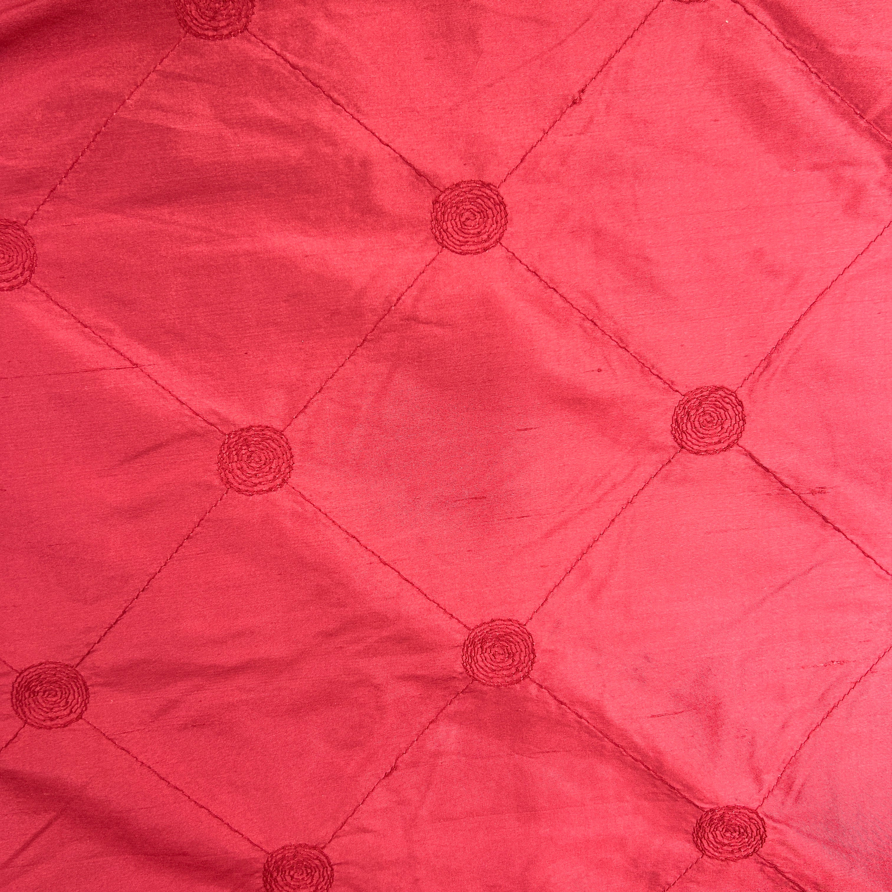 A close-up of a red fabric with a diamond quilted pattern and matching embroidered rosettes.