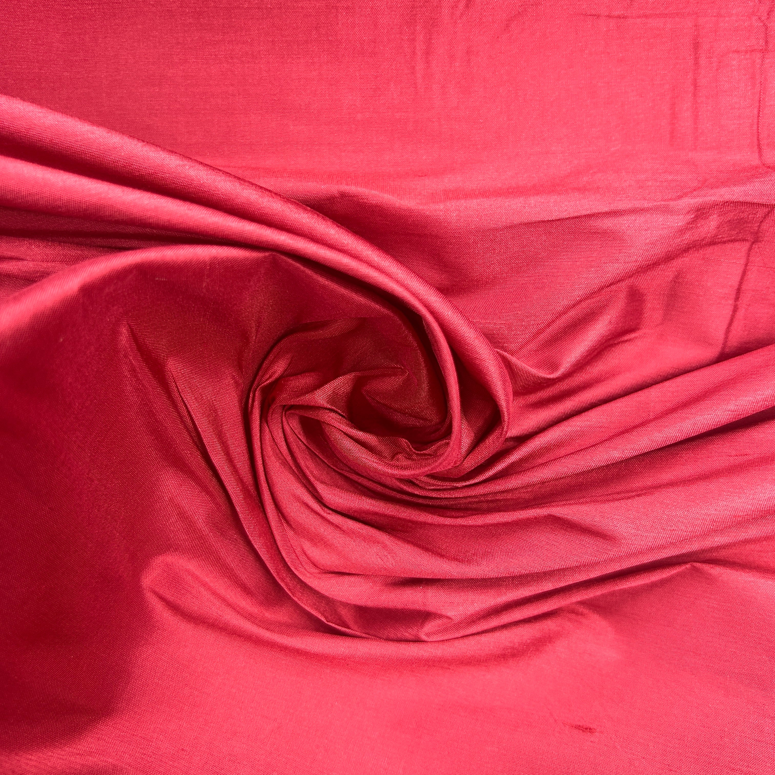 A close-up of bright pink fabric draped in a spiral swirl, showing a smooth satin-like sheen and soft folds.