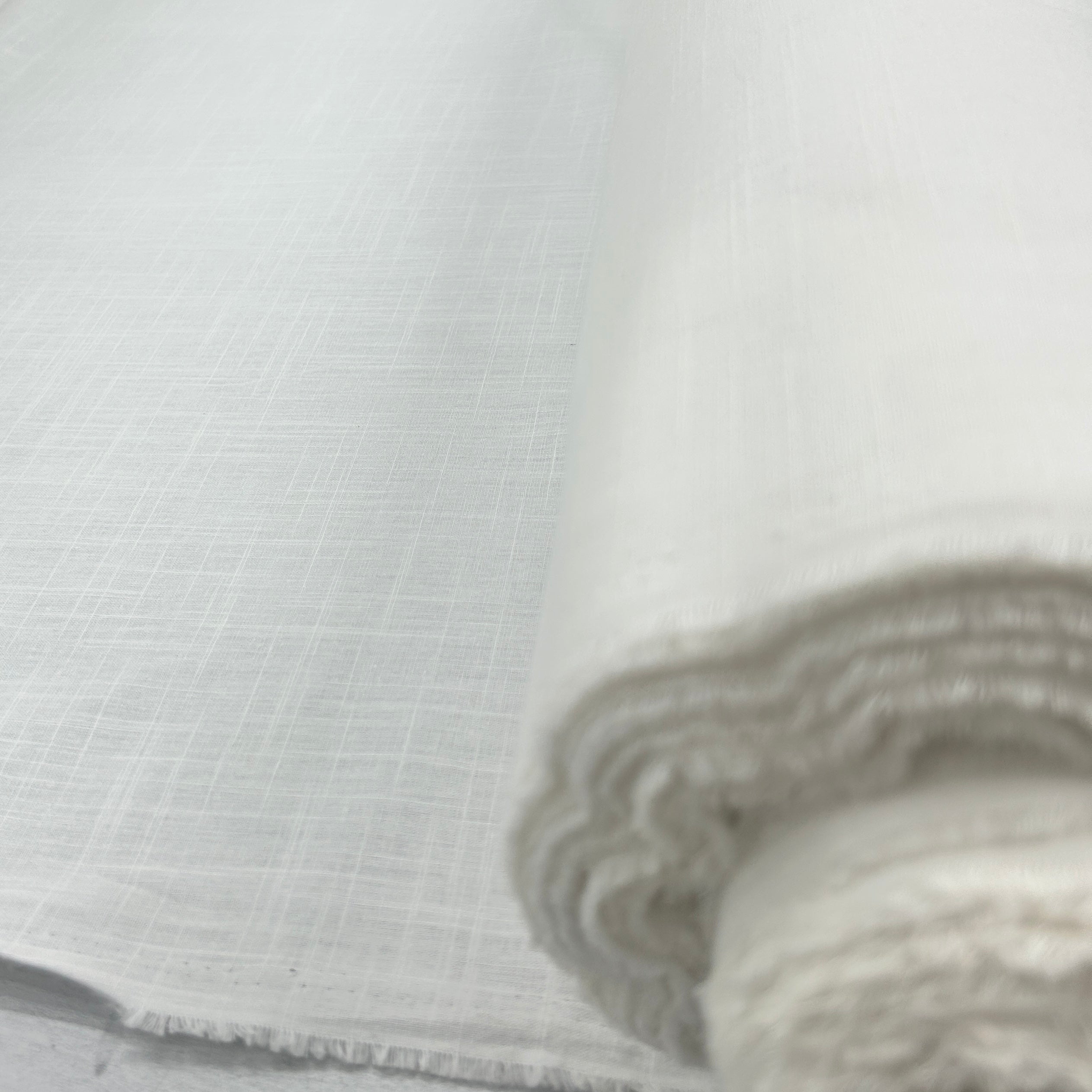 A close-up of a rolled piece of light gray woven fabric, showing its fine texture and frayed edges.