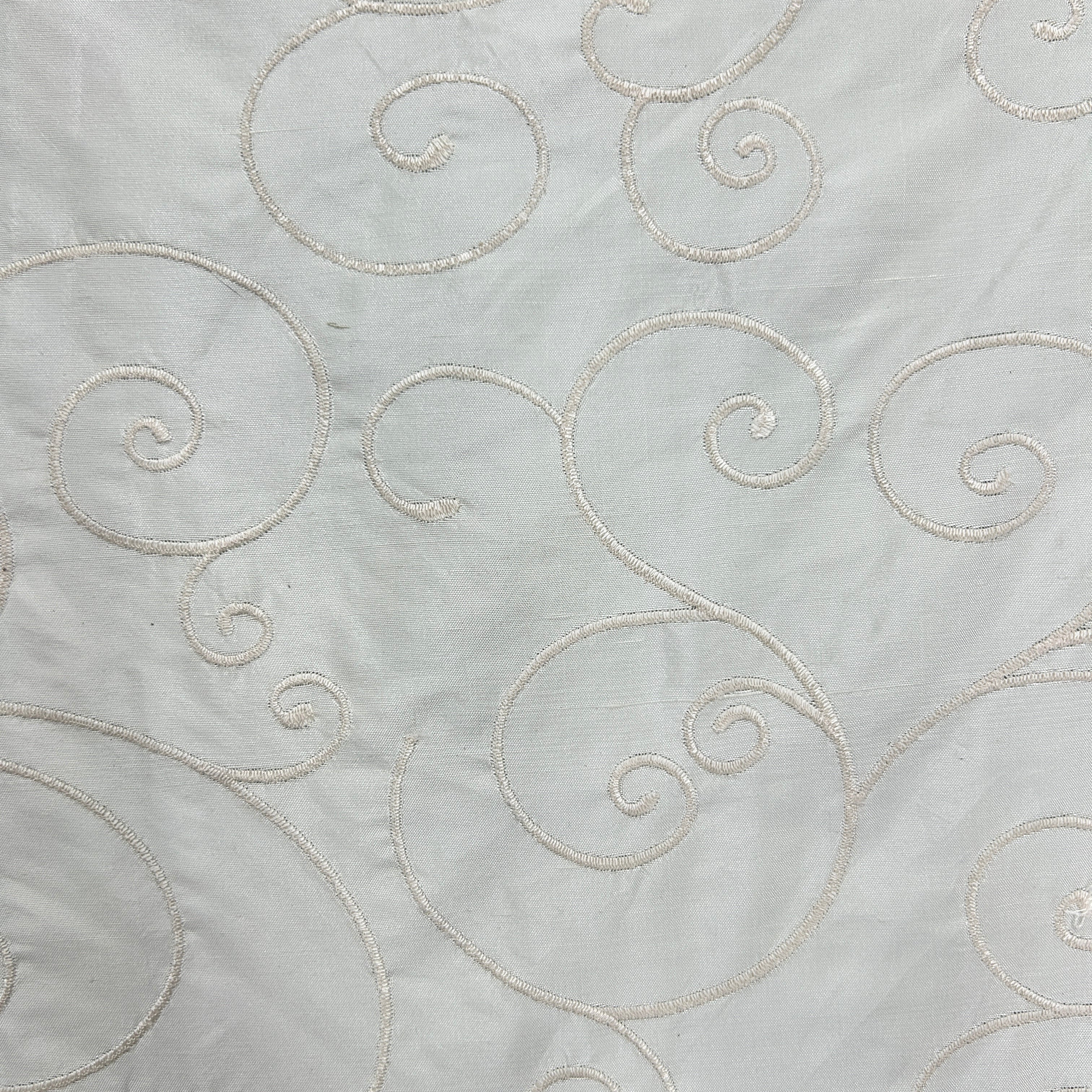White fabric with elegant metallic silver scrollwork embroidery.