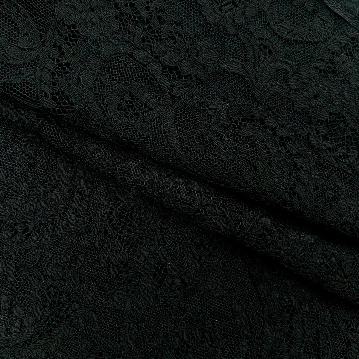 Close-up of black lace fabric with an intricate floral and scroll pattern, draped to show its texture and transparency.