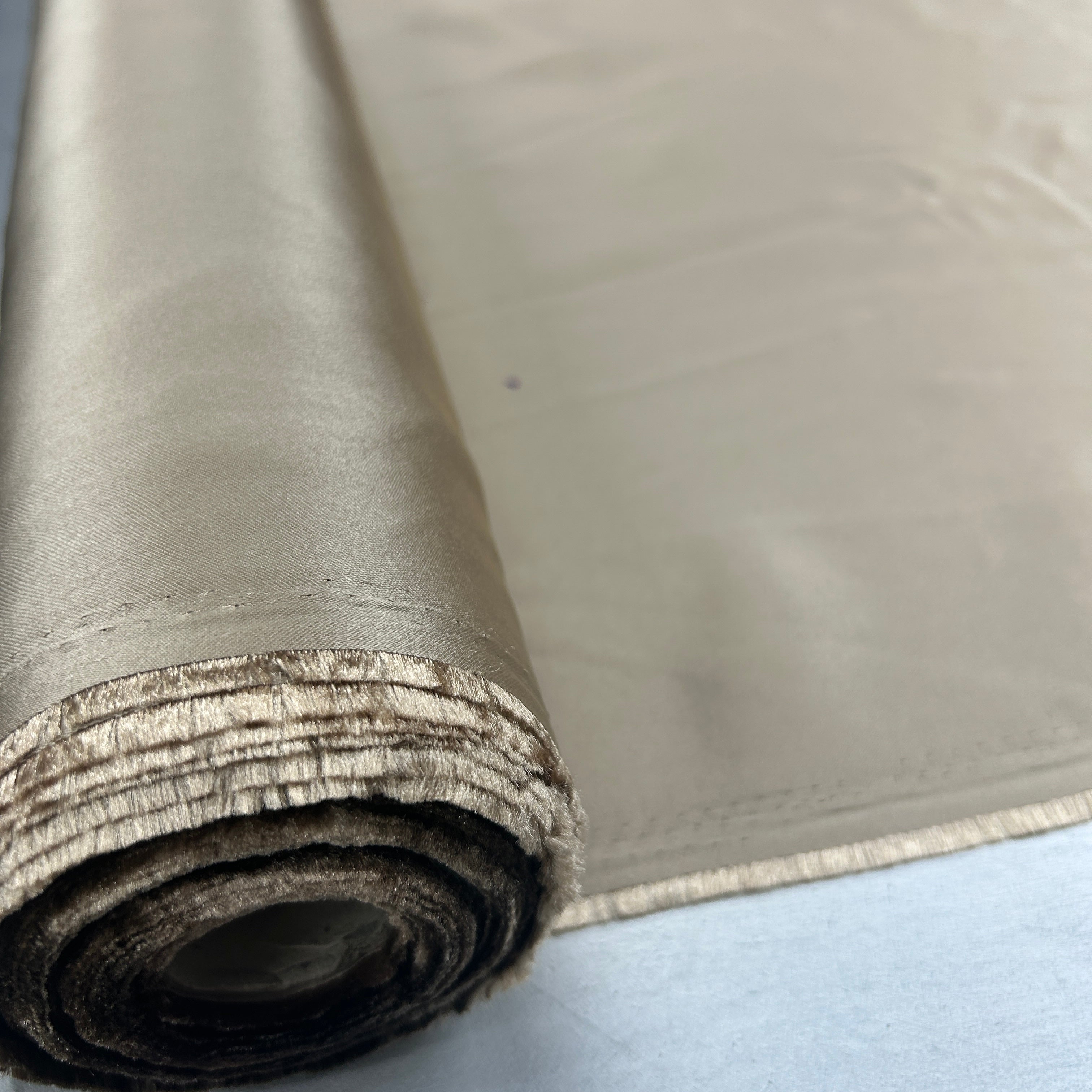 A close-up of a roll of satin fabric, showing its smooth, lustrous surface and layered rolled edges, set against a light blue background.