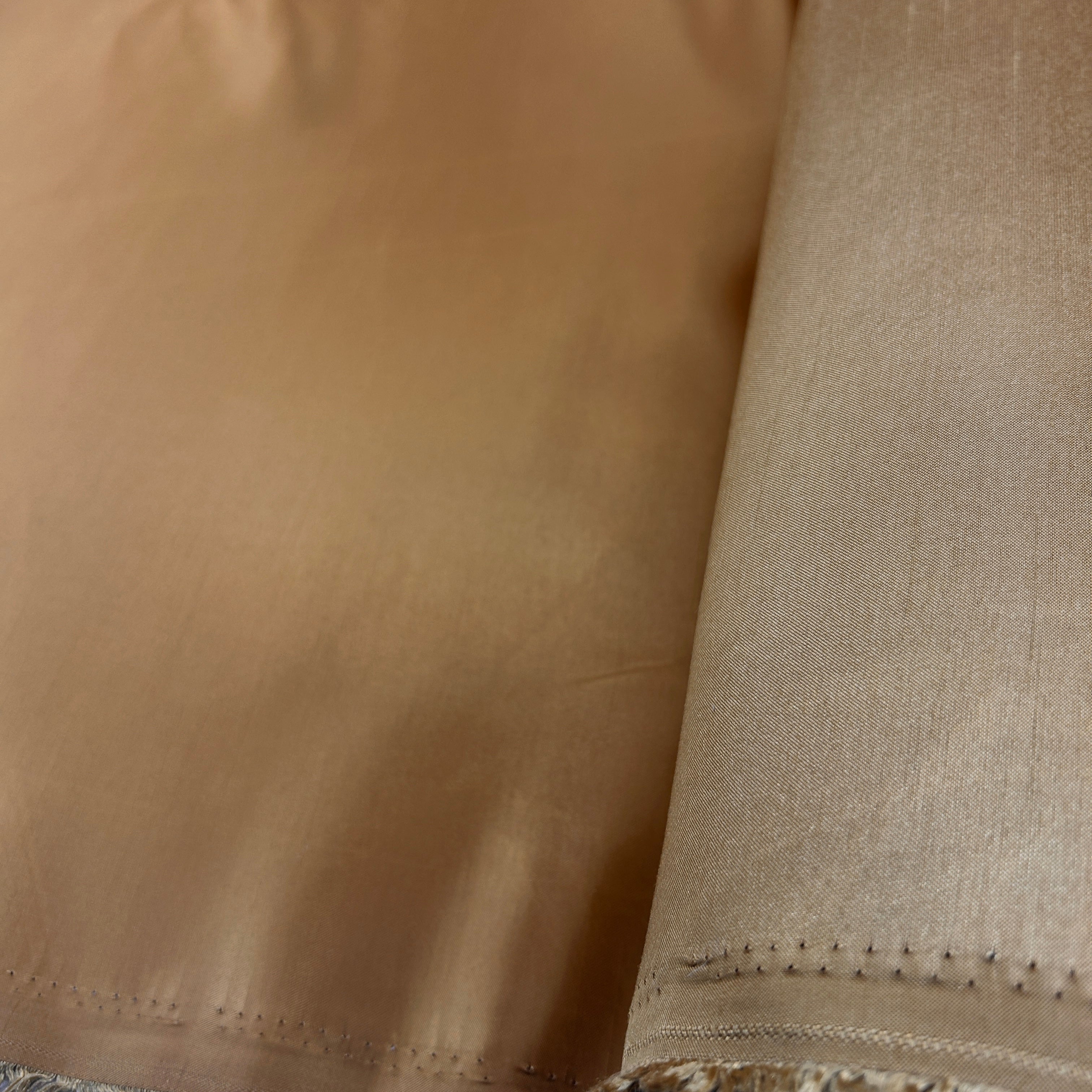 A close-up of a rolled piece of fabric in a warm tan or camel shade, showing the texture and stitched edge.