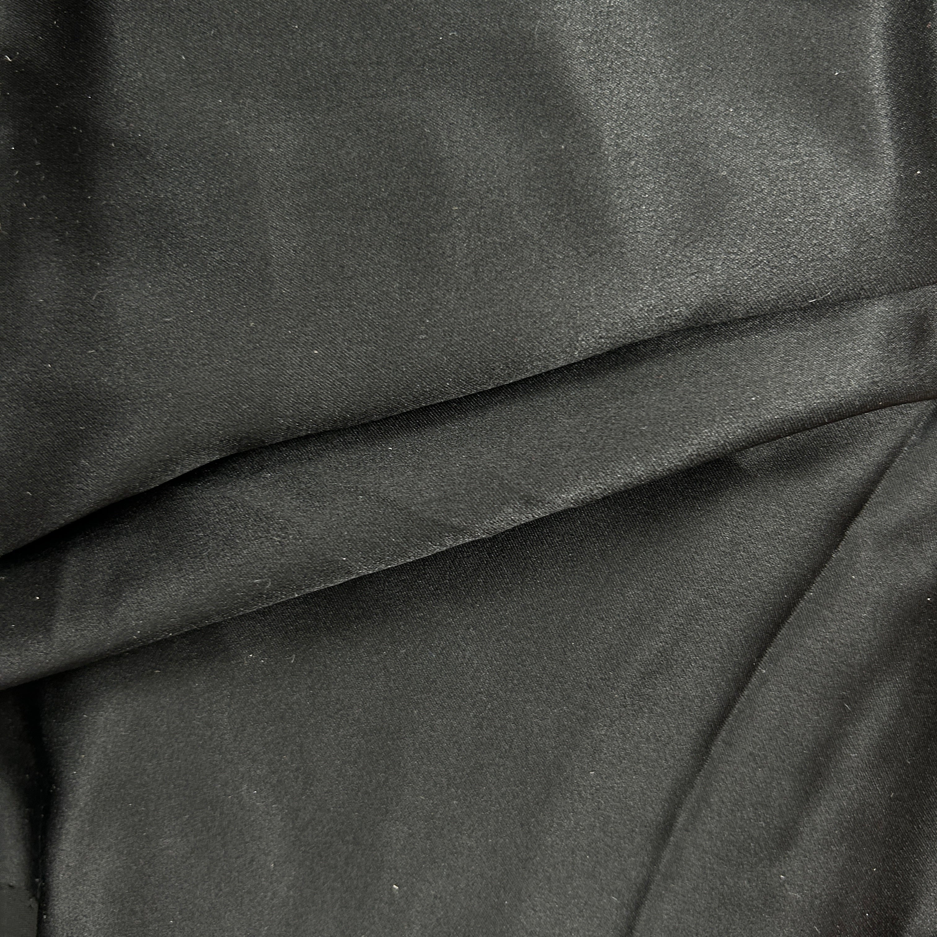 A close-up of draped black fabric with a soft, slightly lustrous texture and gentle folds.