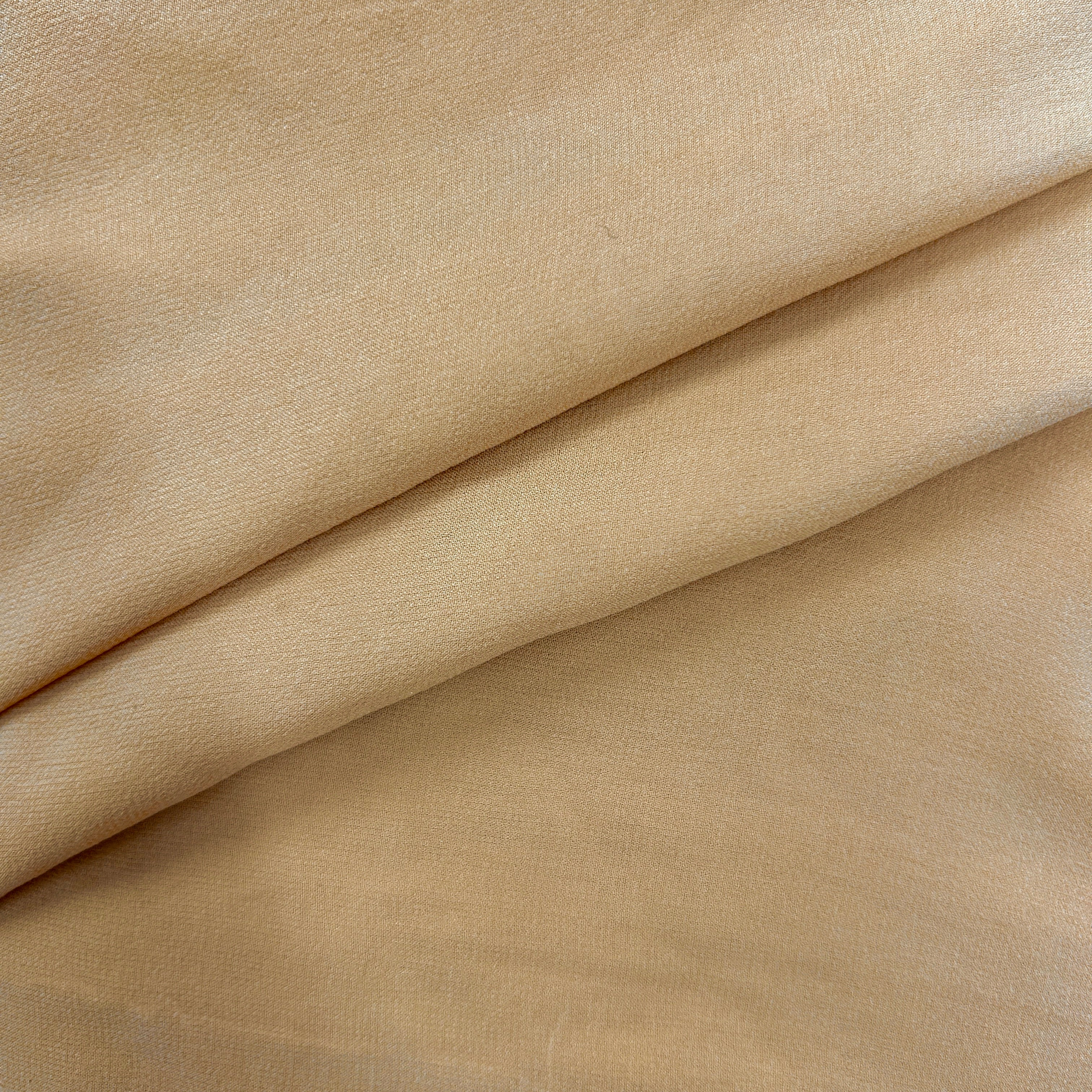 A close-up of draped beige fabric with soft folds and a smooth, slightly lustrous texture.