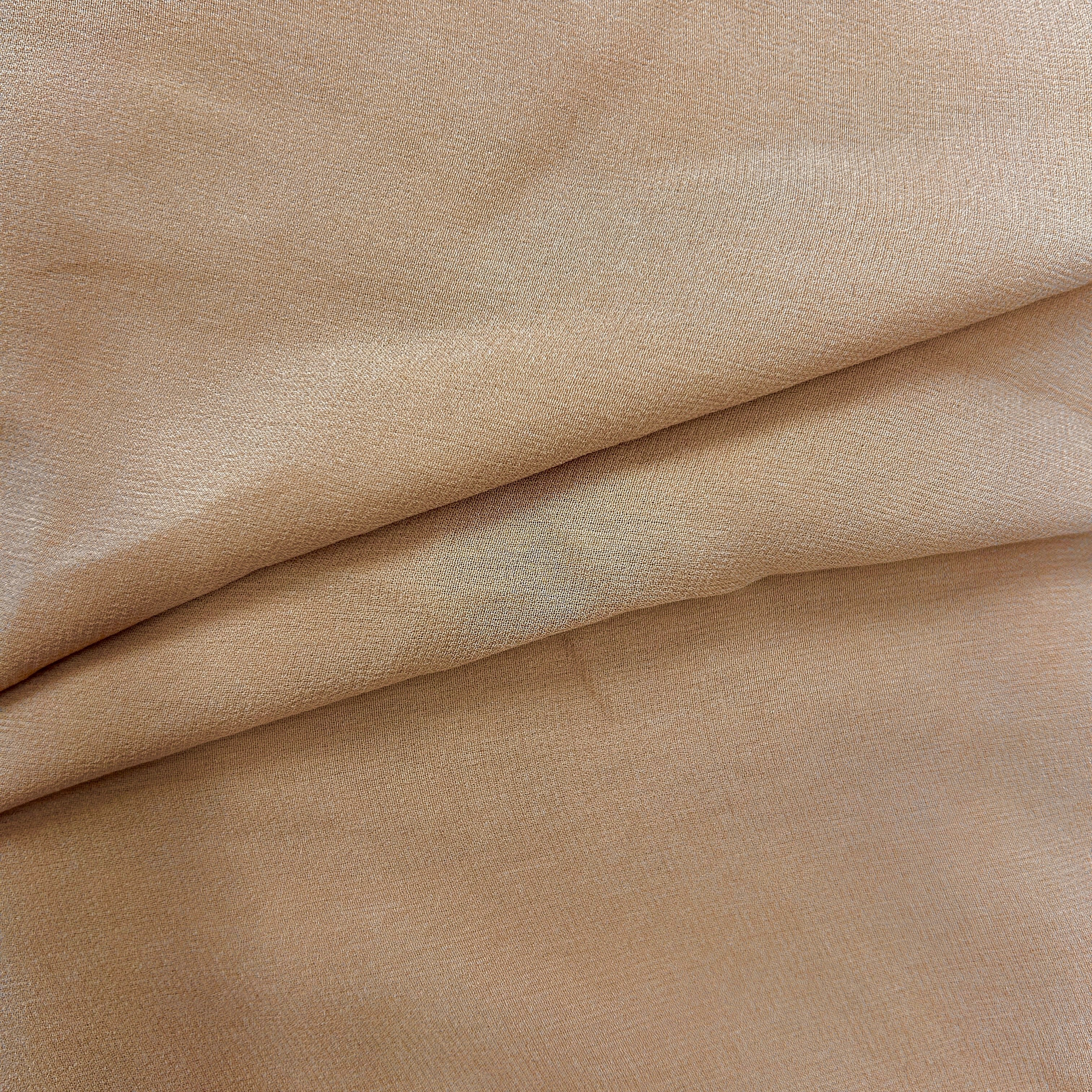 A close-up of draped beige fabric with a fine woven texture and soft folds.
