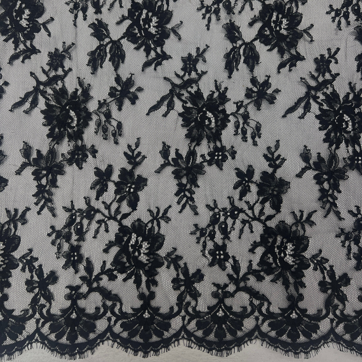 Black floral lace fabric with a scalloped edge, shown laid flat against a white background.