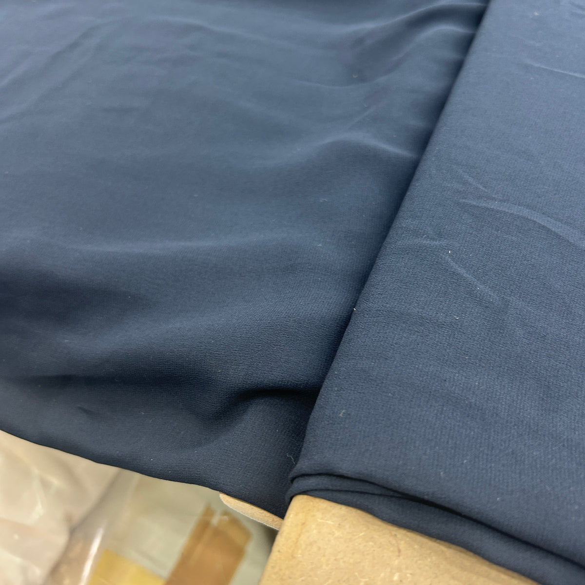 A close-up of folded navy blue fabric, showing its texture and color, resting on a light-colored surface.