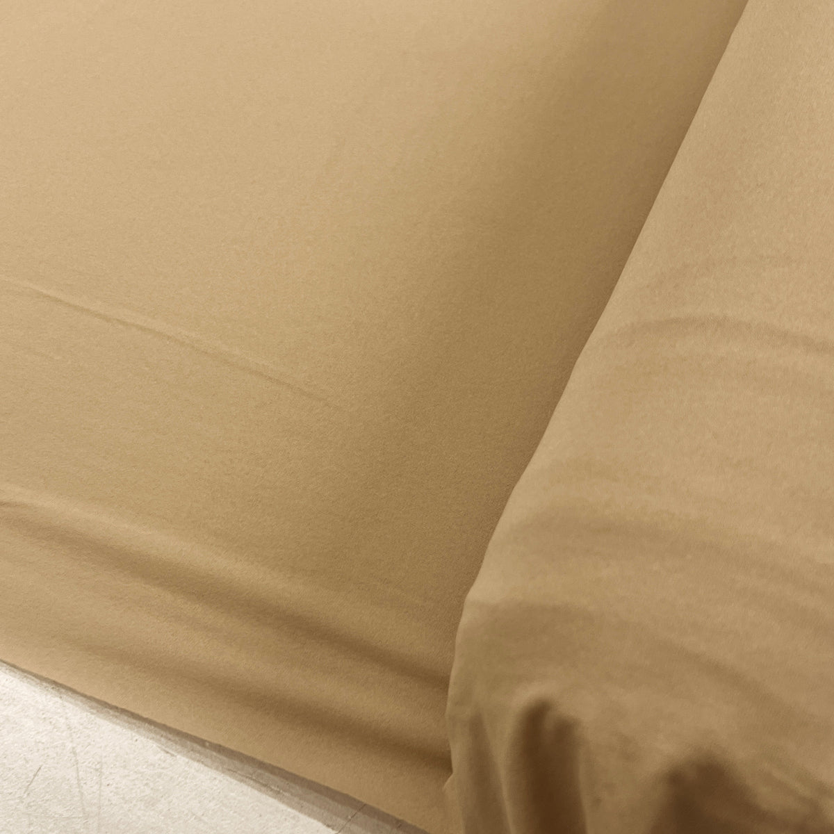 A close-up of a beige or tan fabric sheet or bedding corner with a rolled edge, showing the material texture and color.