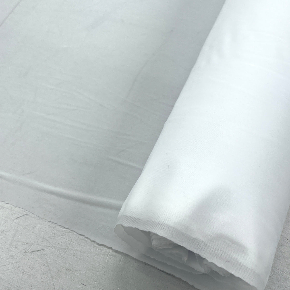 A roll of white fabric or plastic sheeting partially unrolled on a light gray surface.