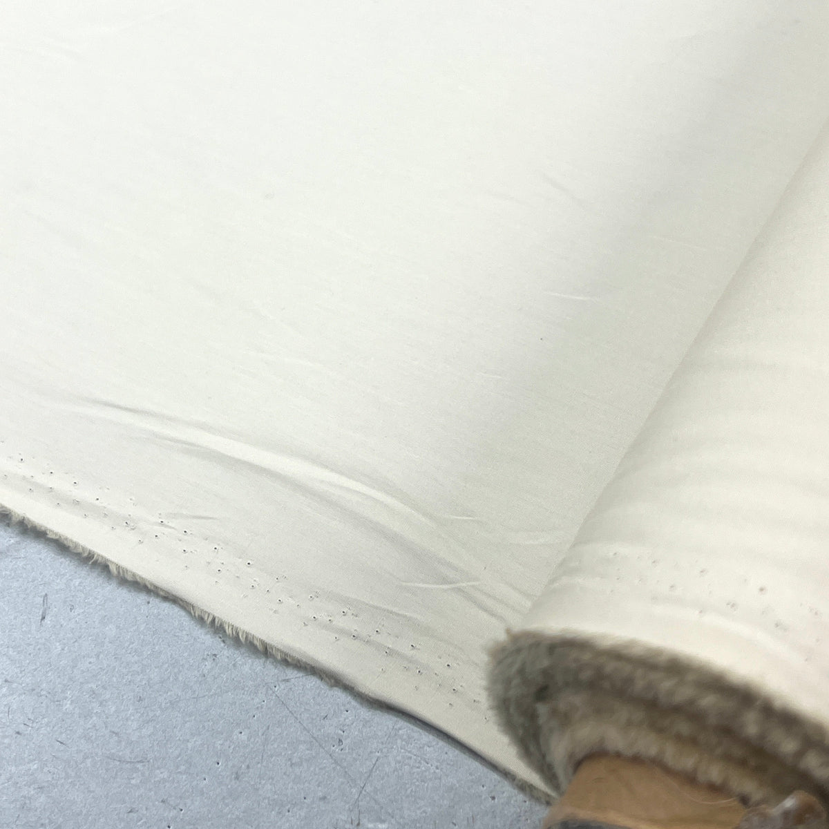 A close-up of a rolled piece of off-white fabric or paper, showing the textured surface and folded edge, resting on a gray surface.