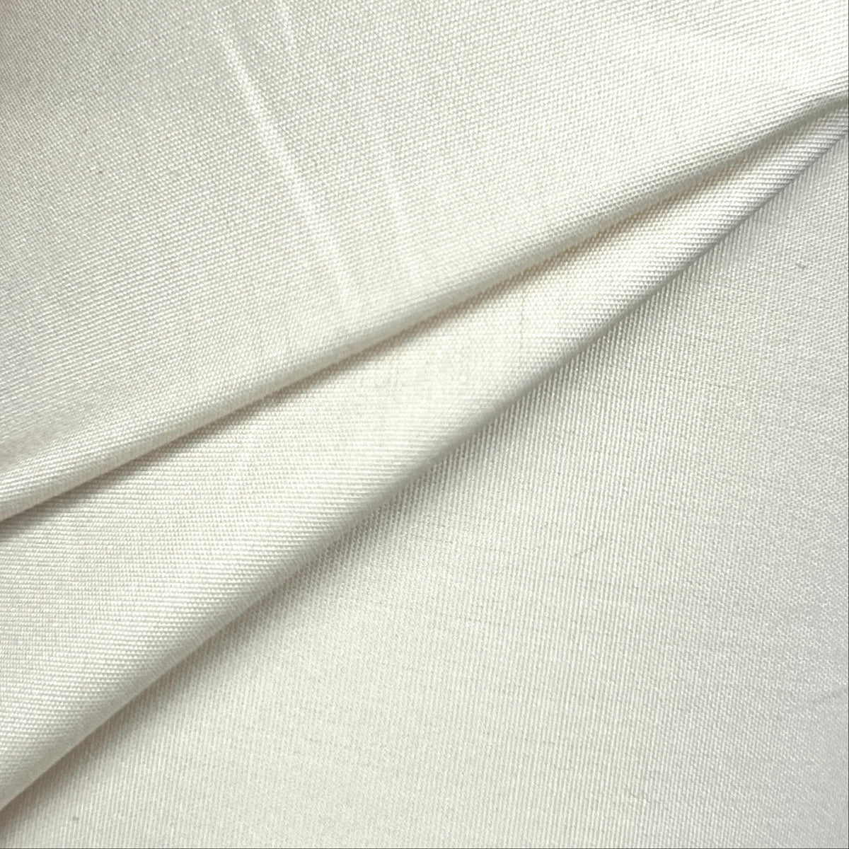 A close-up of off-white fabric being held by a hand, showing its soft texture and folds.