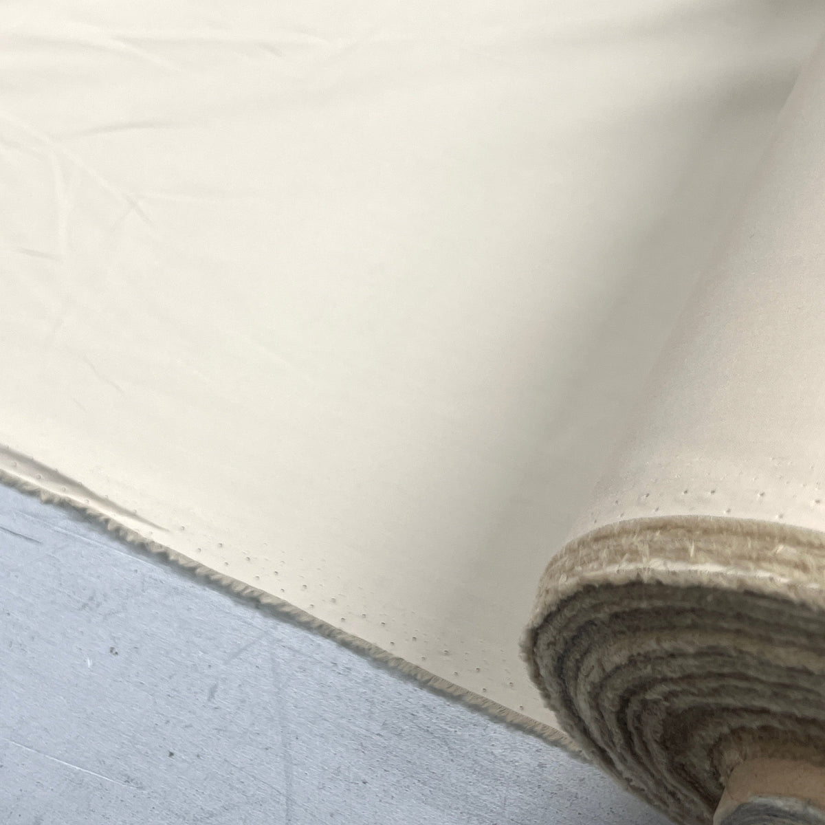 A close-up of a rolled cream-colored fabric or material, showing its texture and edge, laid over a gray surface.