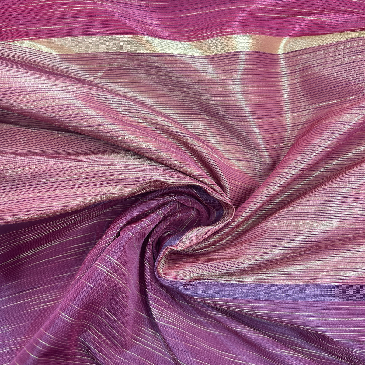A close-up of a draped fabric with a shimmering magenta and purple colorway, featuring fine horizontal metallic gold stripes and a central swirl.