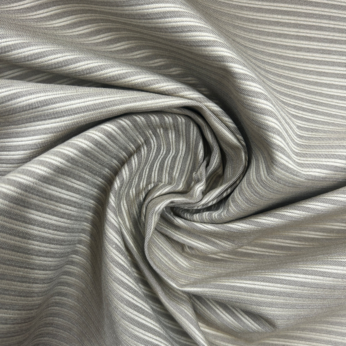 A close-up of draped fabric with a fine striped pattern in gray and white, arranged in a spiral to show the material's texture and drape.