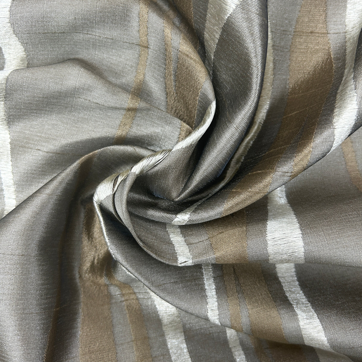 A close-up of draped striped fabric with a shimmering metallic finish, featuring vertical stripes in taupe, beige, white, and gray.