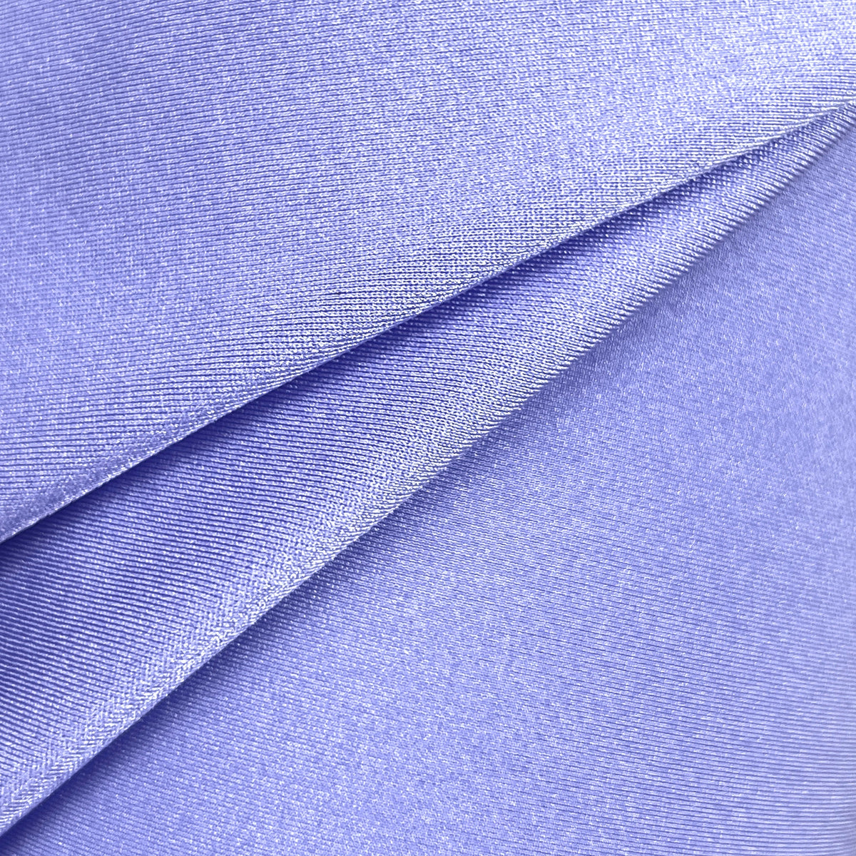A close-up of draped lavender fabric with a fine textured weave, showing soft folds and a subtle sheen against a white background.