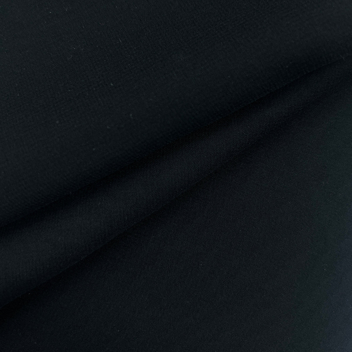 A close-up of black fabric with soft folds and a subtle woven texture.