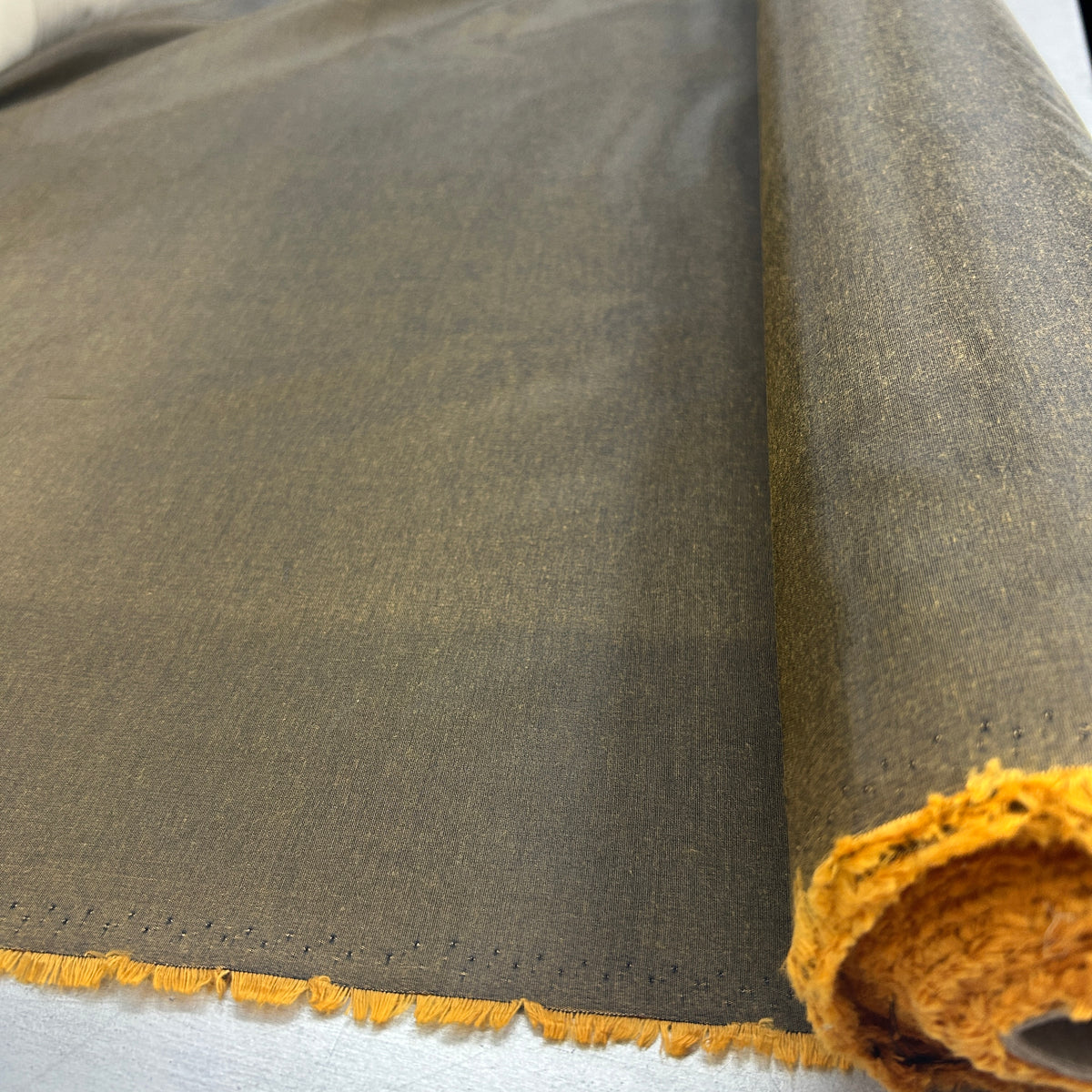 A close-up of a rolled piece of textured fabric in a muted olive-brown color, showing a contrasting mustard-yellow frayed edge and the rolled underside.