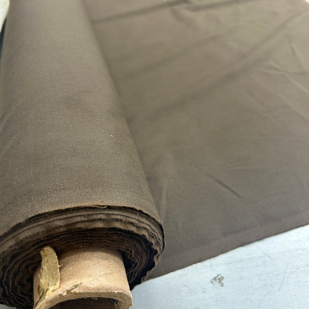 A close-up of a roll of dark brown fabric, partially unrolled to show its texture and color, mounted on a cardboard core.