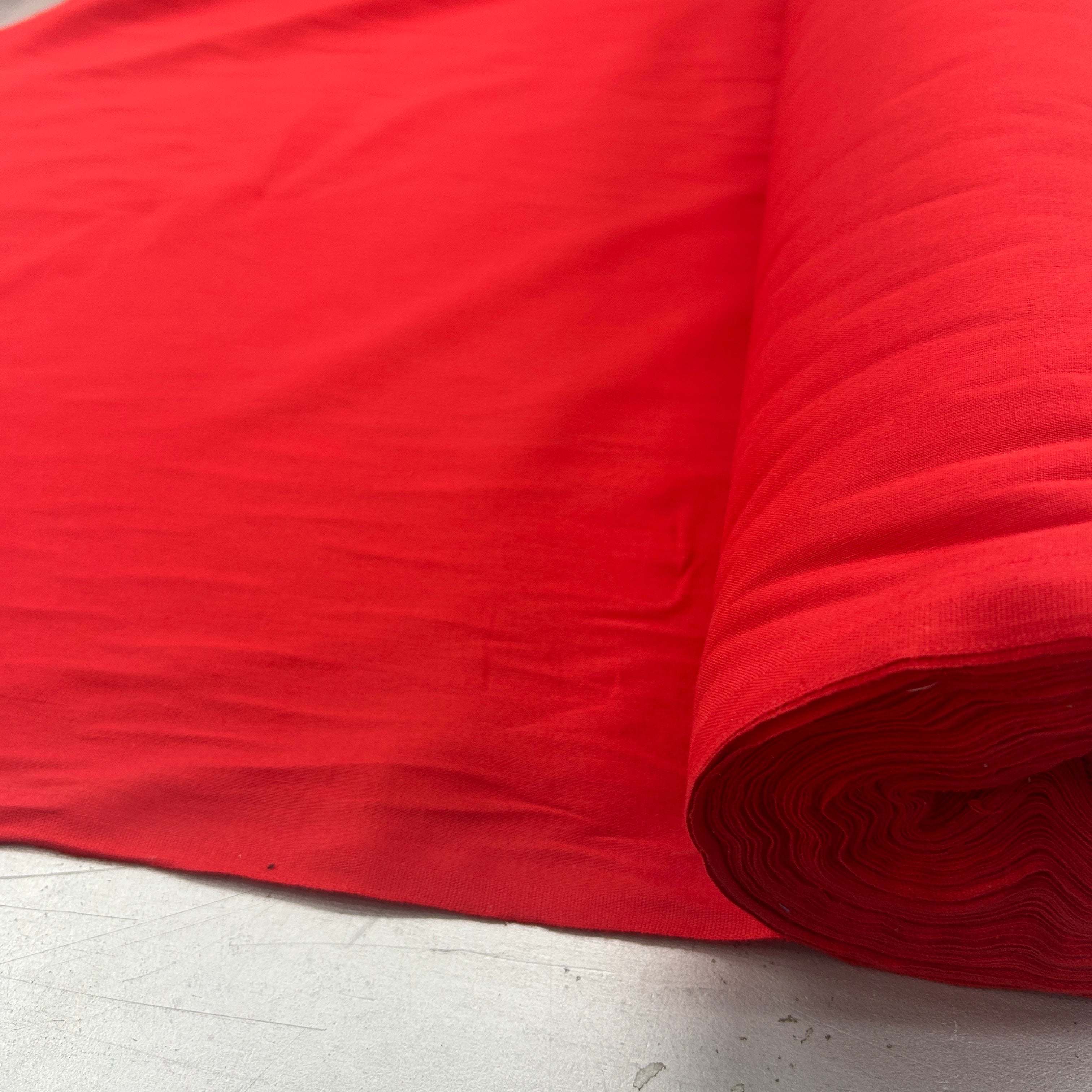 A bright red roll of fabric or material spread out on a light gray surface, with the roll visible on the right side.