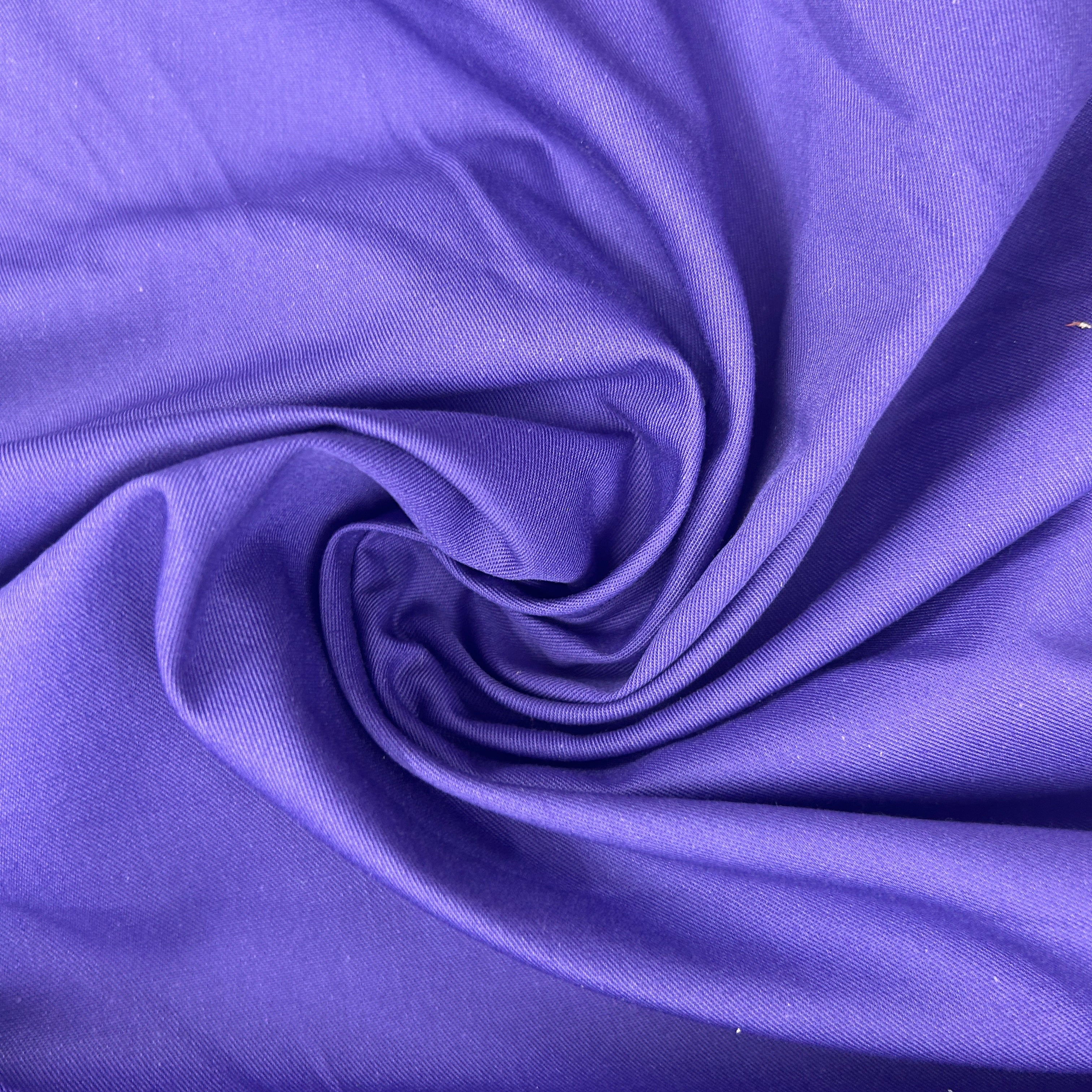 A close-up of purple fabric arranged in a spiral drape, showing the material texture and color.