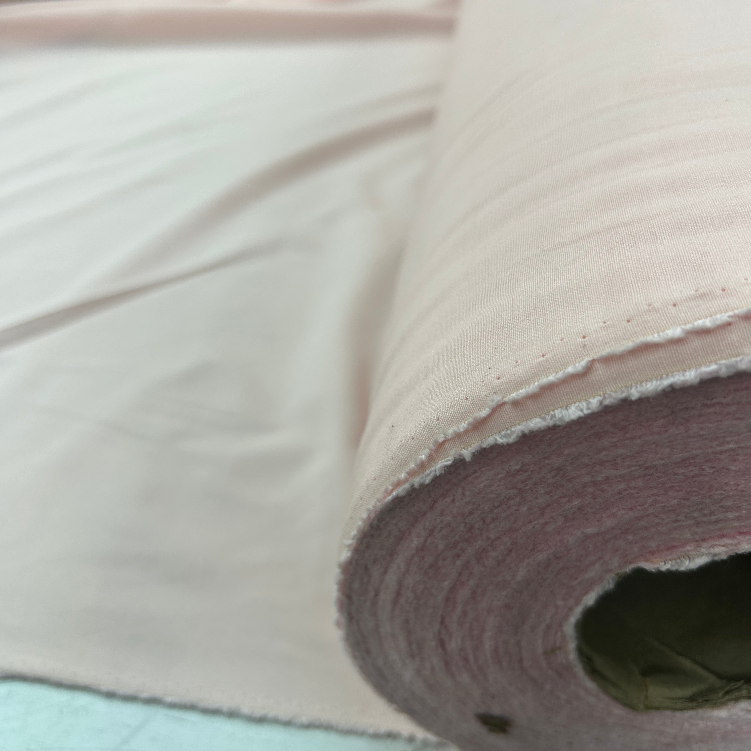 A close-up of a roll of light pink fabric, showing its texture and color as it is unrolled.