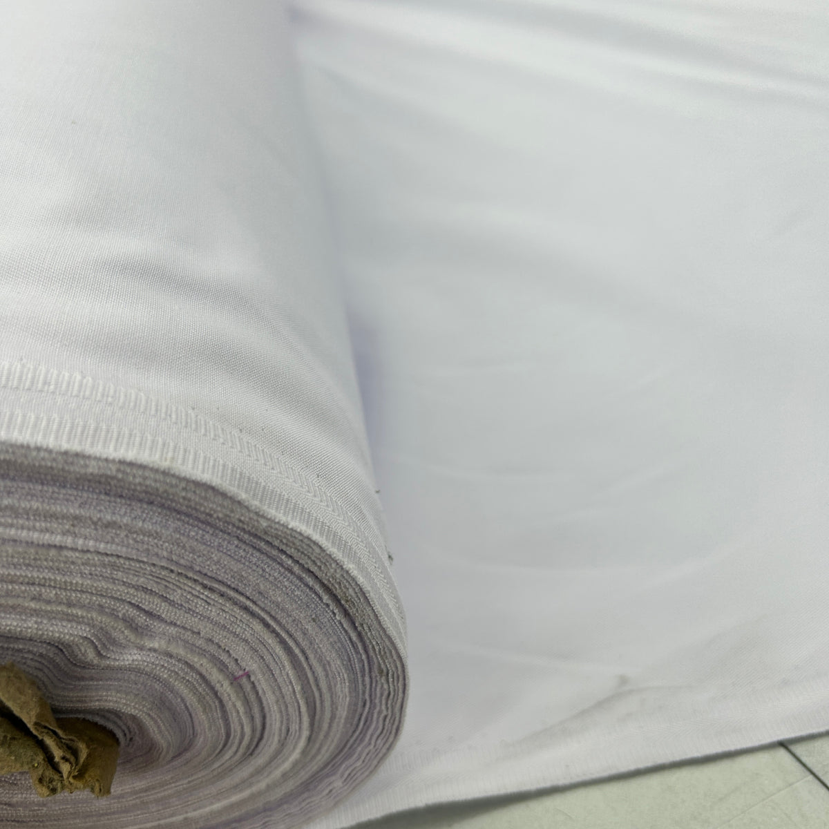 A close-up of a white fabric roll with a ribbed hem, showing the layered texture of the material as it is unrolled.