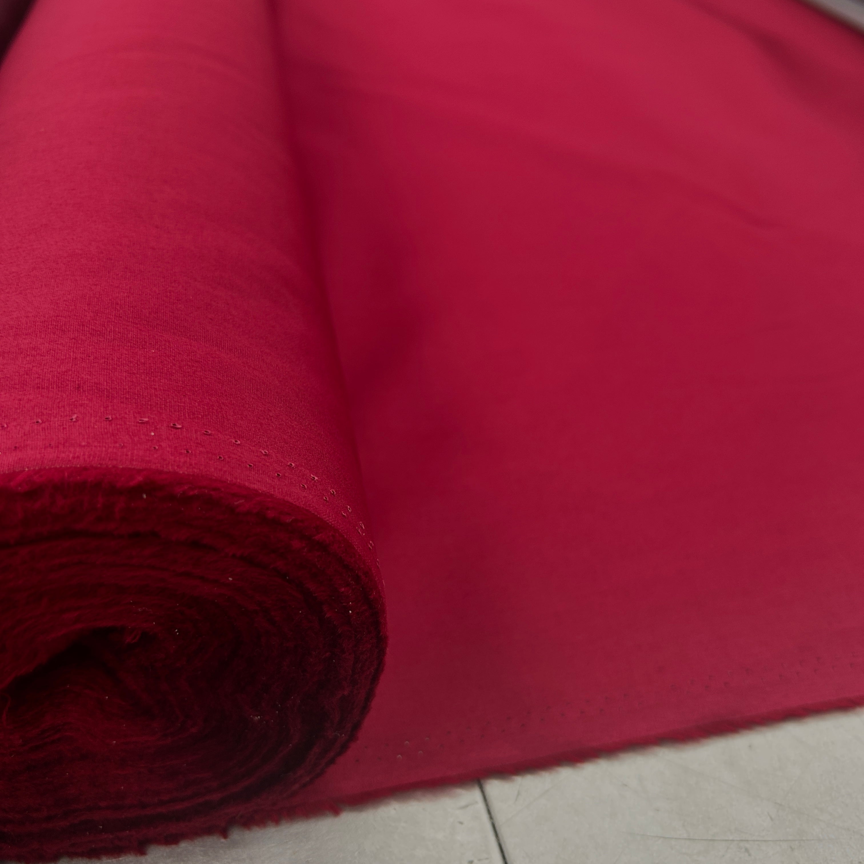 A close-up of a rolled piece of bright red fabric, showing its texture and color, laid next to a light gray tiled floor.