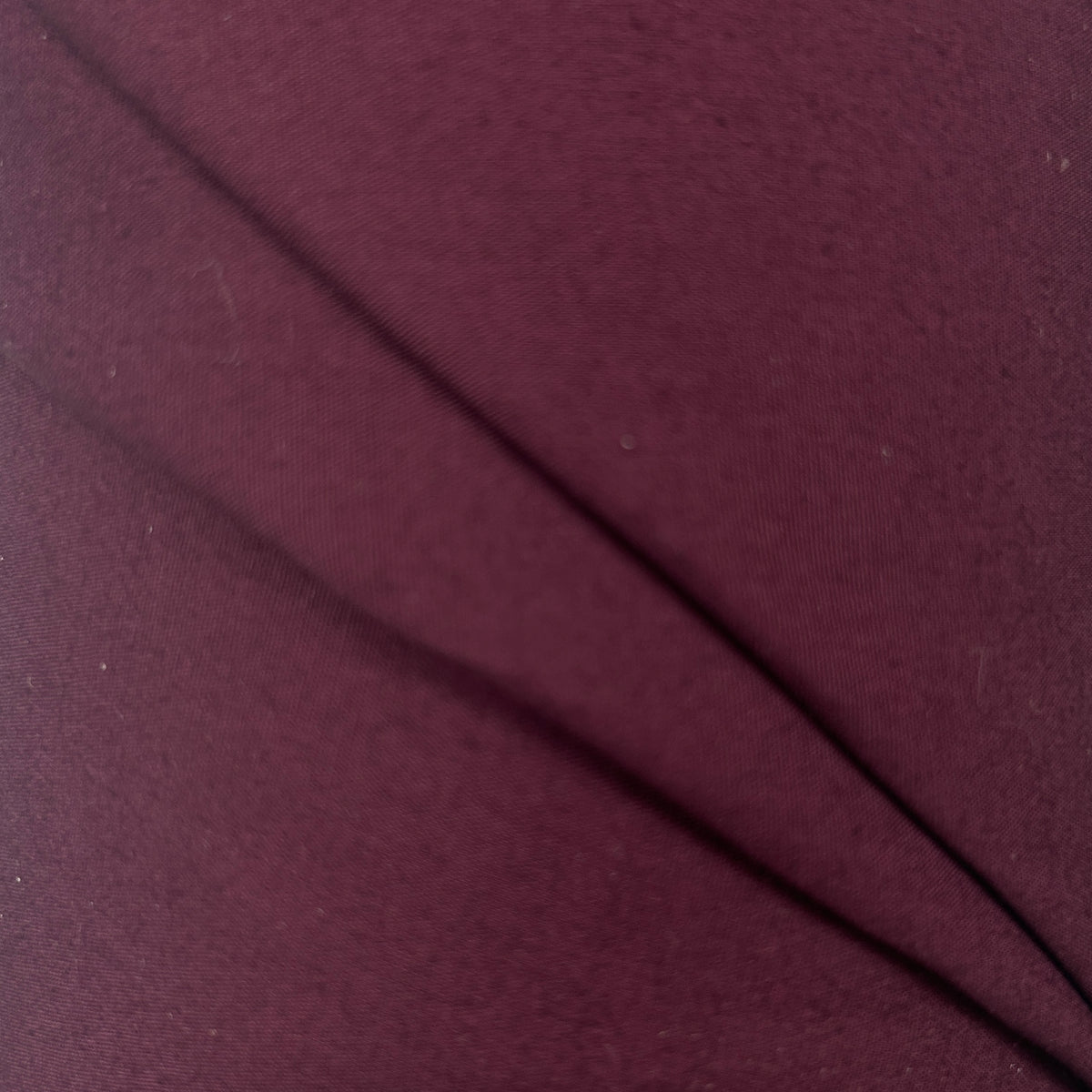 A close-up of a dark burgundy or plum-colored fabric with a fine ribbed texture and a diagonal seam running across the frame.
