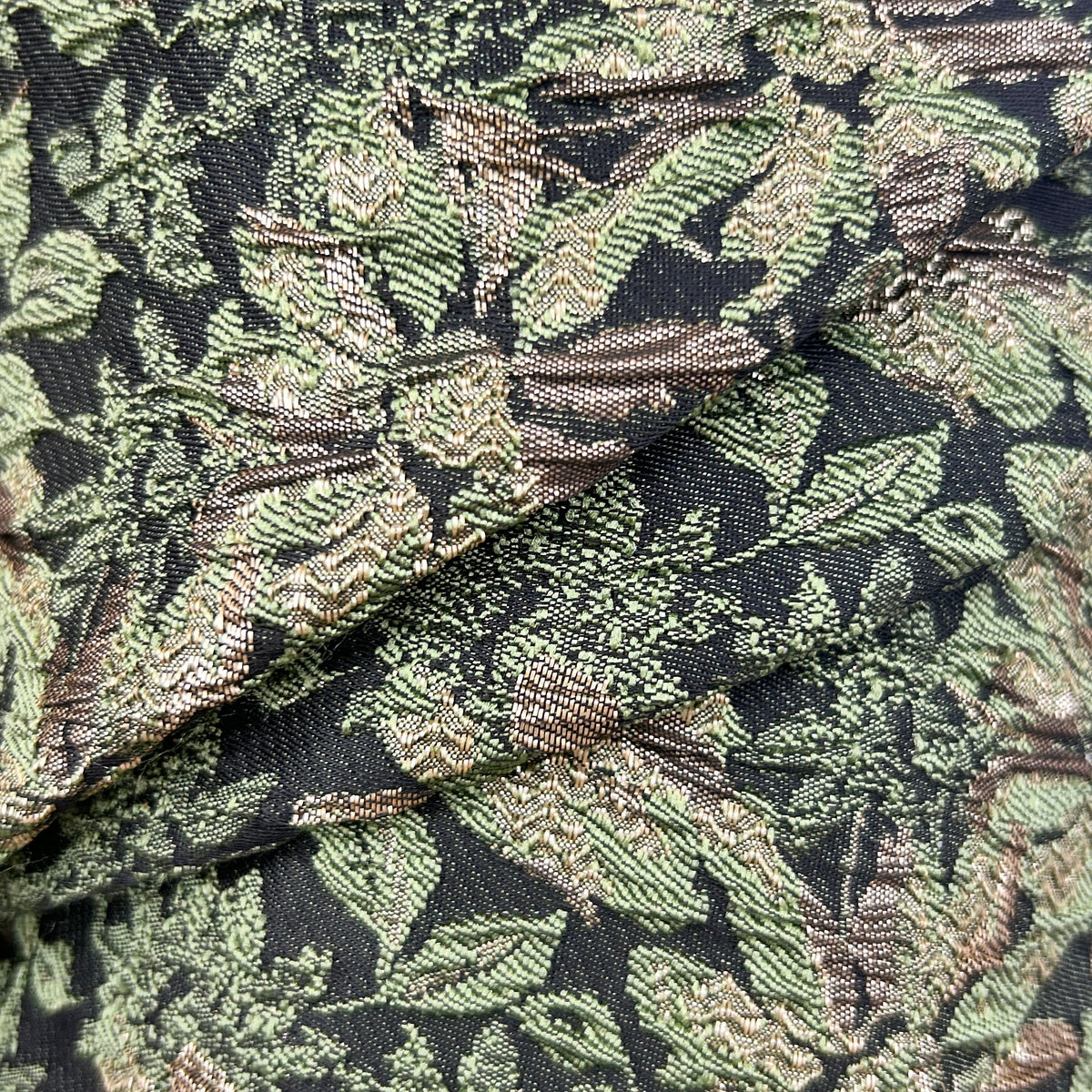 Close-up of green brocade floral upholstery fabric with intricate leaf and flower patterns.