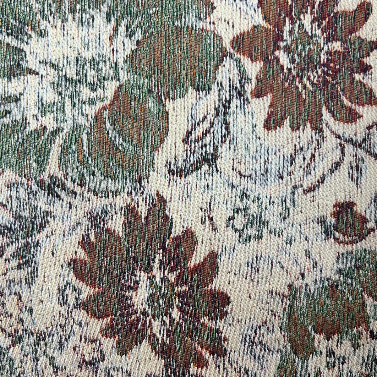 A close-up of a woven fabric with a distressed floral pattern in muted green, brown, and gray on an off-white background.