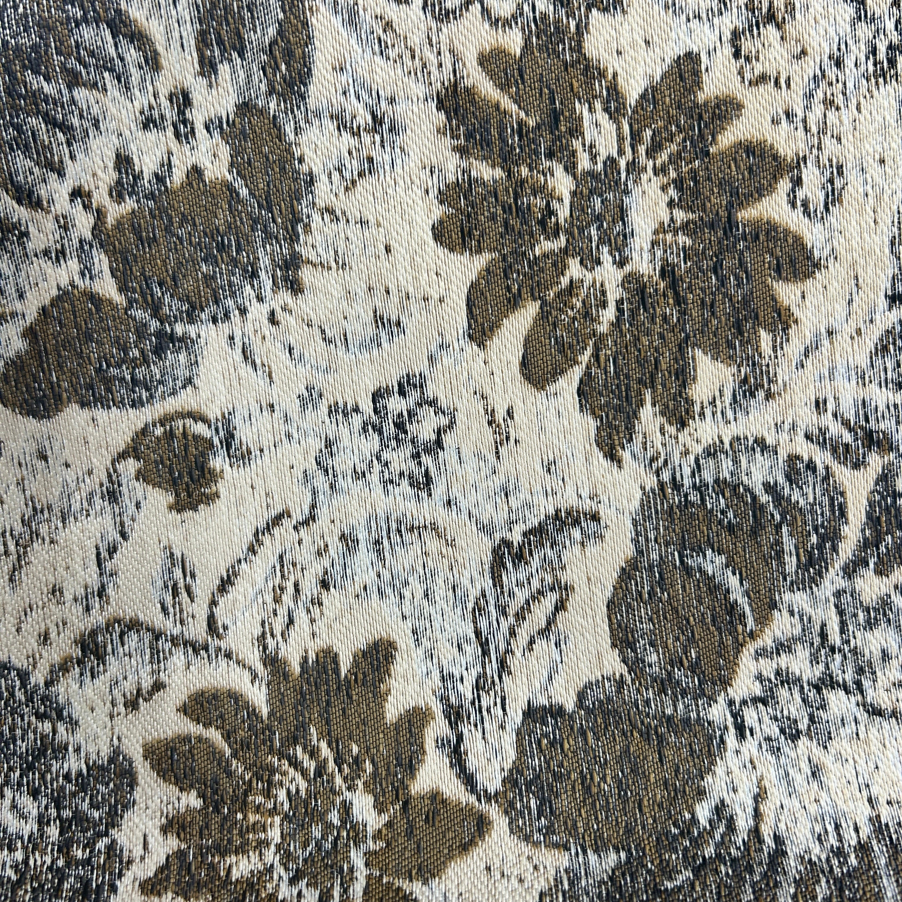 A close-up of a woven fabric or rug pattern featuring large distressed floral motifs in dark brown and gray on an off-white background.