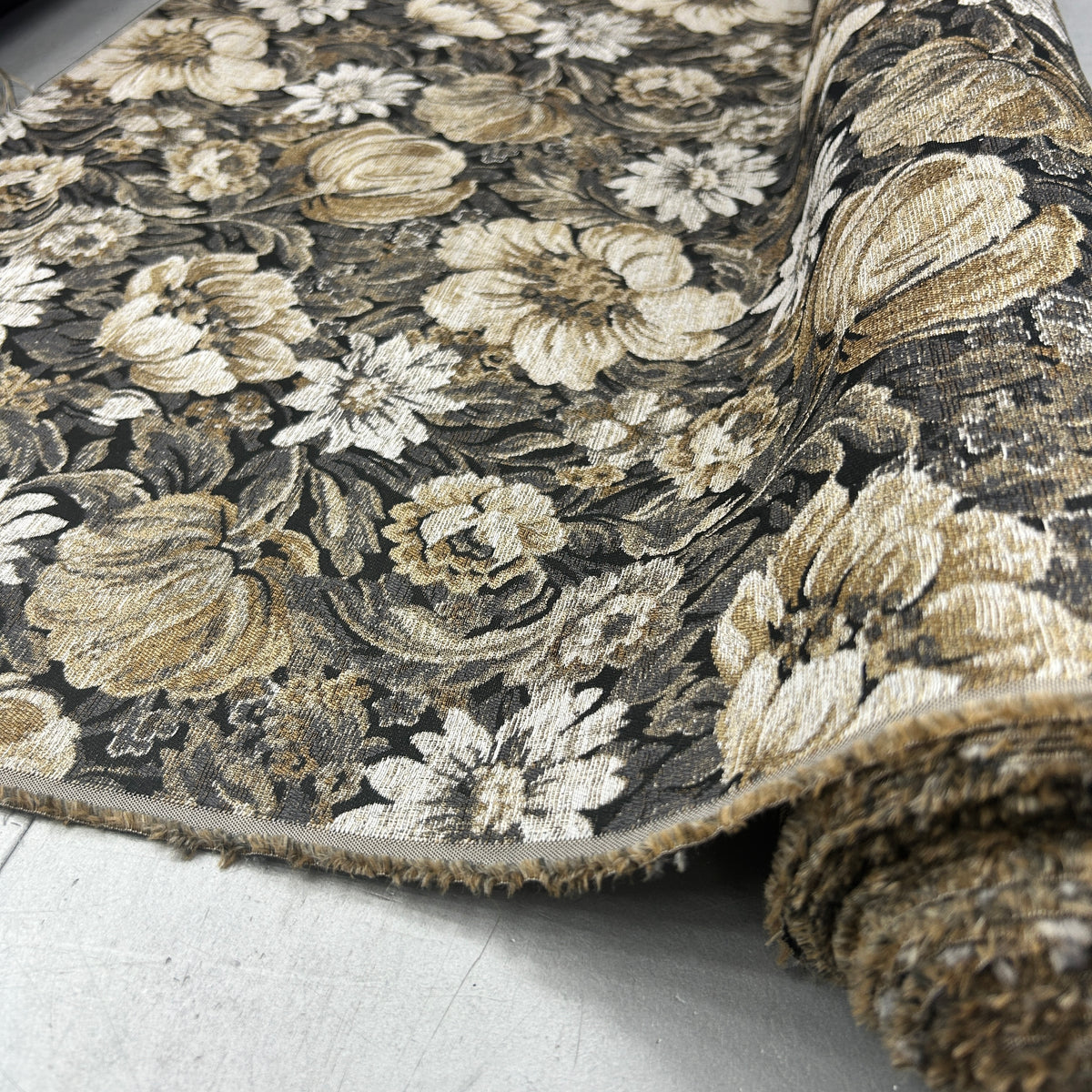 A close-up of a rolled area rug showing its detailed floral and pumpkin pattern in beige, cream, and brown tones against a dark charcoal background.